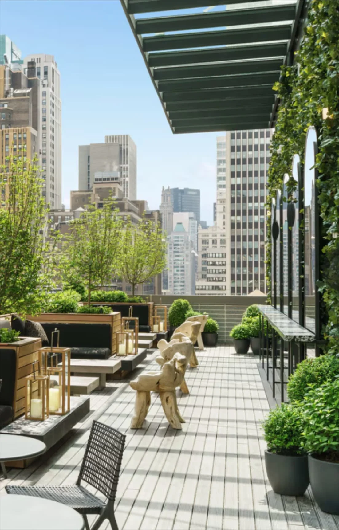Rooftop terrace with greenery, modern seating, and city skyscrapers in the background on a clear day.