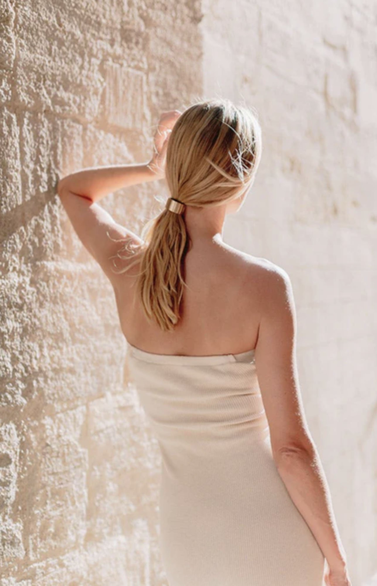 woman facing away leaning on a stone wall