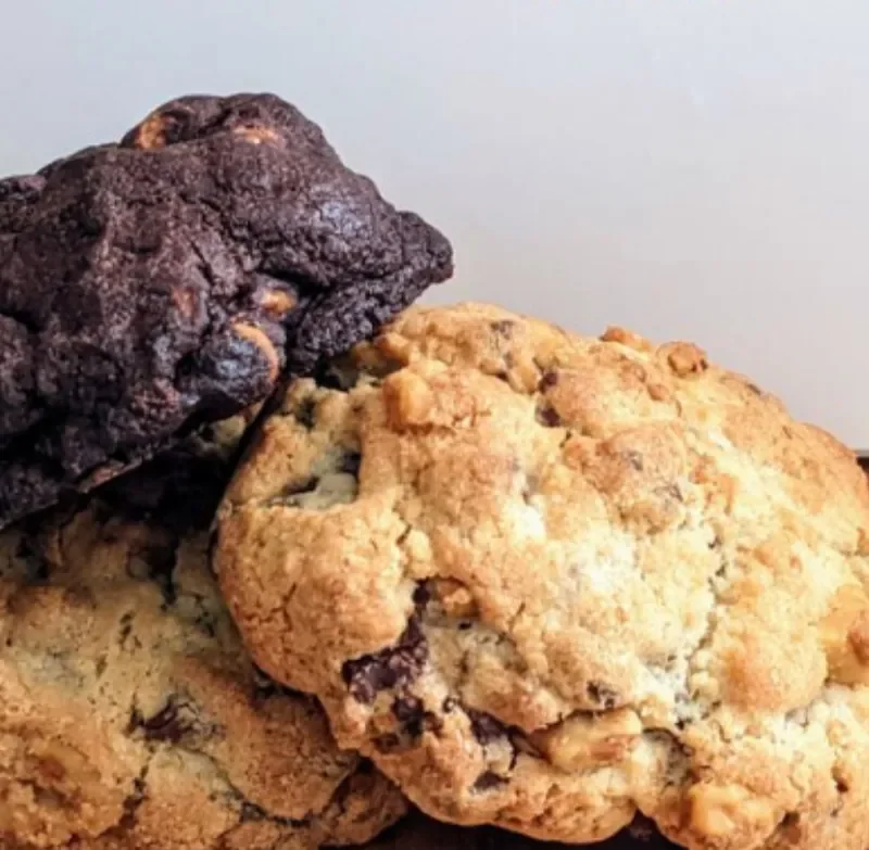 Close-up of three freshly baked chocolate chip cookies, one with dark chocolate and walnuts, one with white chocolate and macadamia nuts, and one with milk chocolate chips.