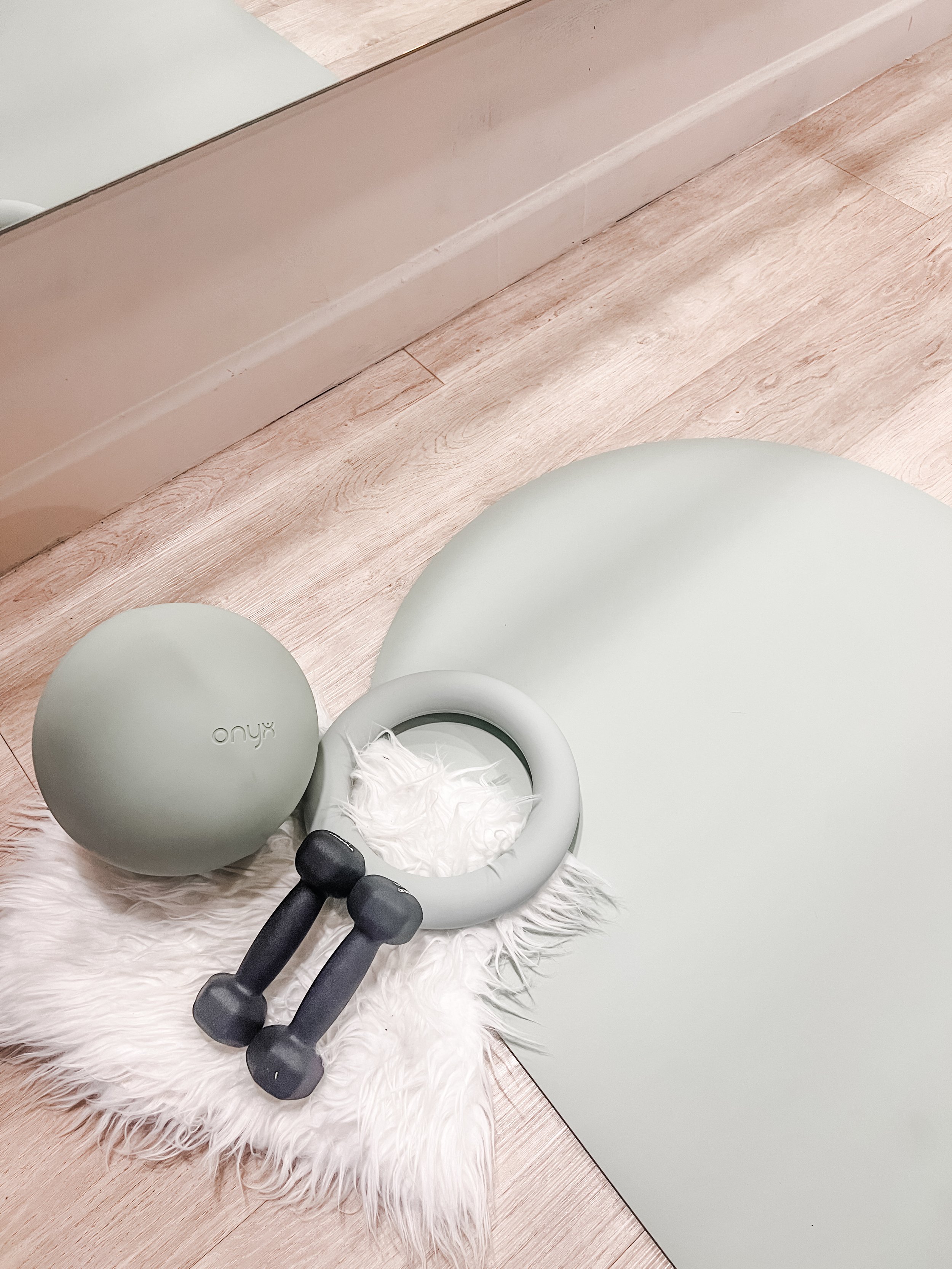 Green Pilates class equipment including a kettlebell, bottle, headband, and a towel with the letters 'M.O' on a cream-colored surface.