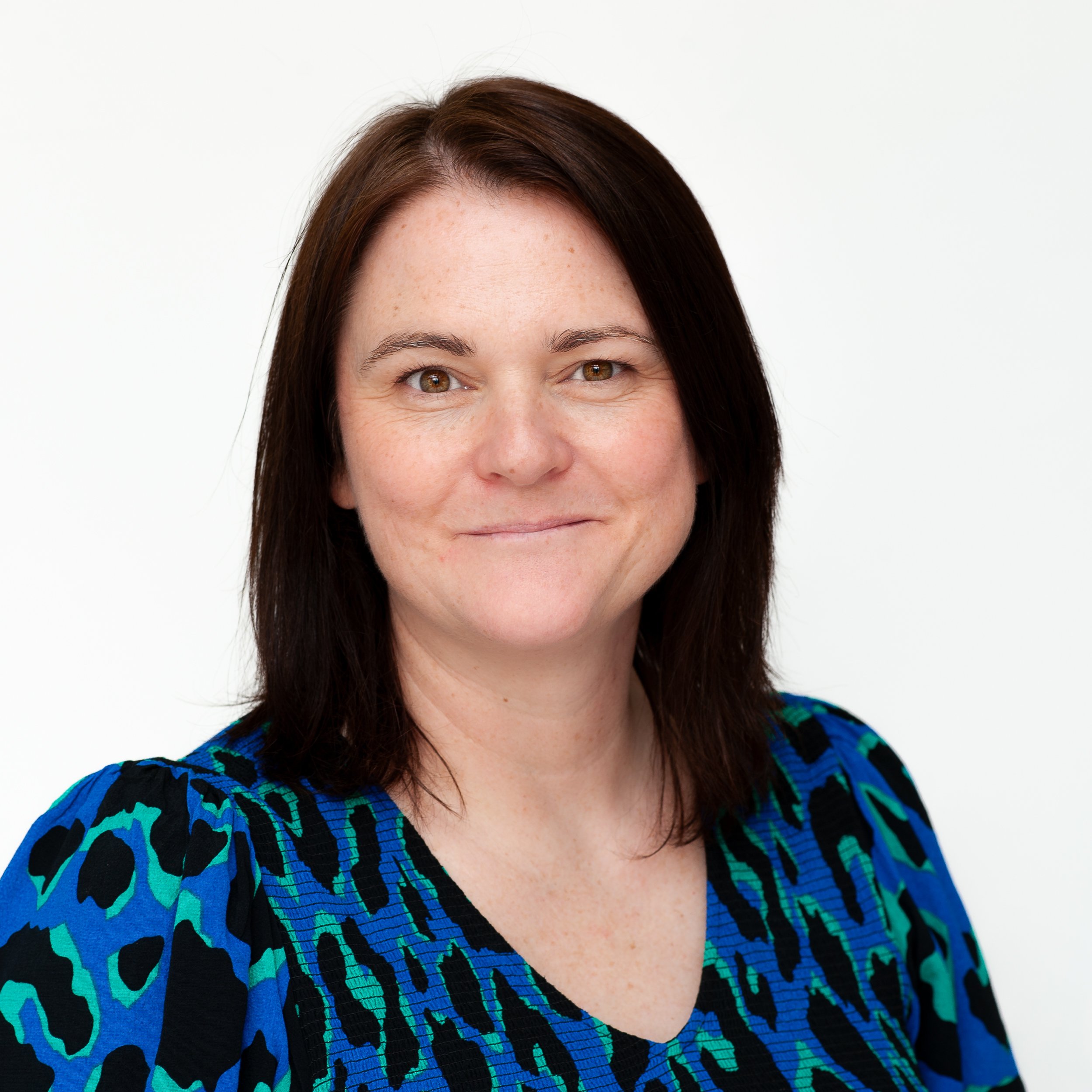 Smiling woman with brown hair in a blue patterned top against a white background.