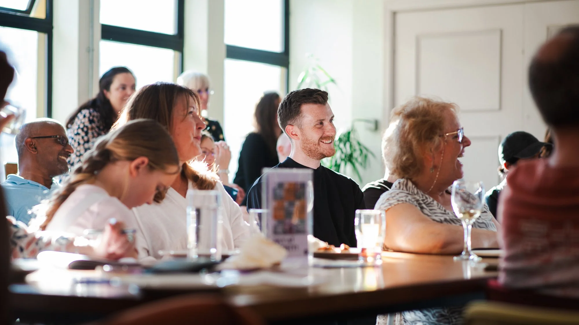 Group of people sitting at a table, smiling and enjoying a gathering indoors.