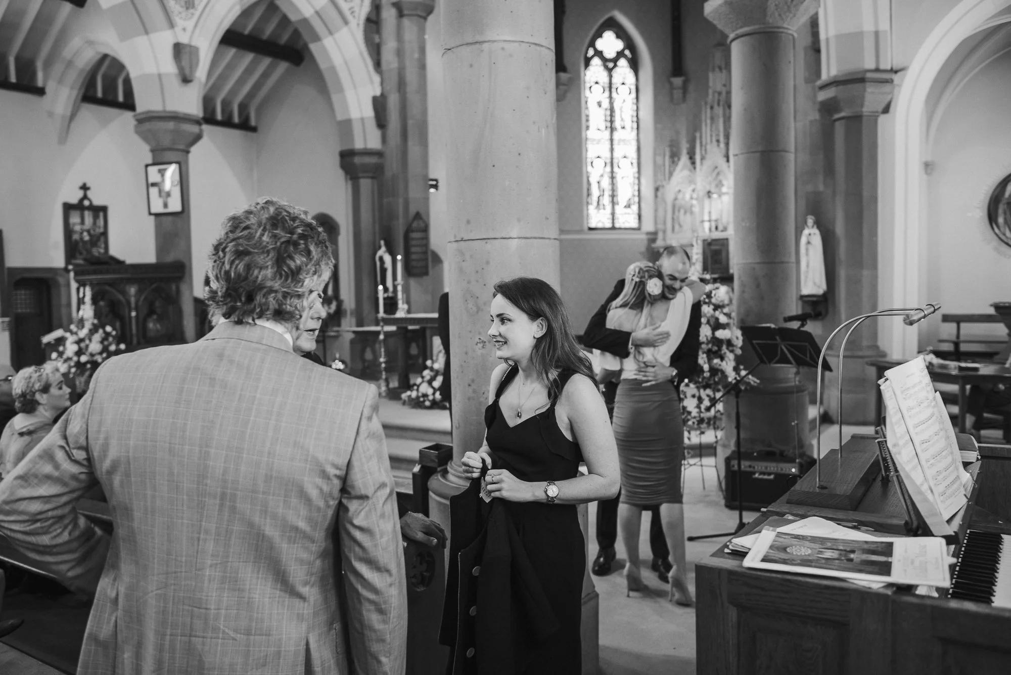 People inside a church, with two women and a man standing near an altar, smiling and hugging, during a wedding ceremony.