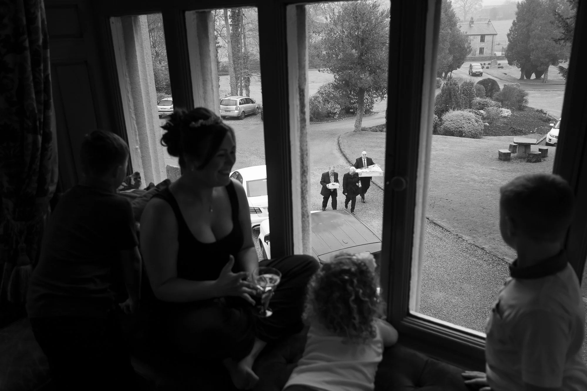 People sitting and standing near a large window looking outside, with three individuals carrying food trays from outside.