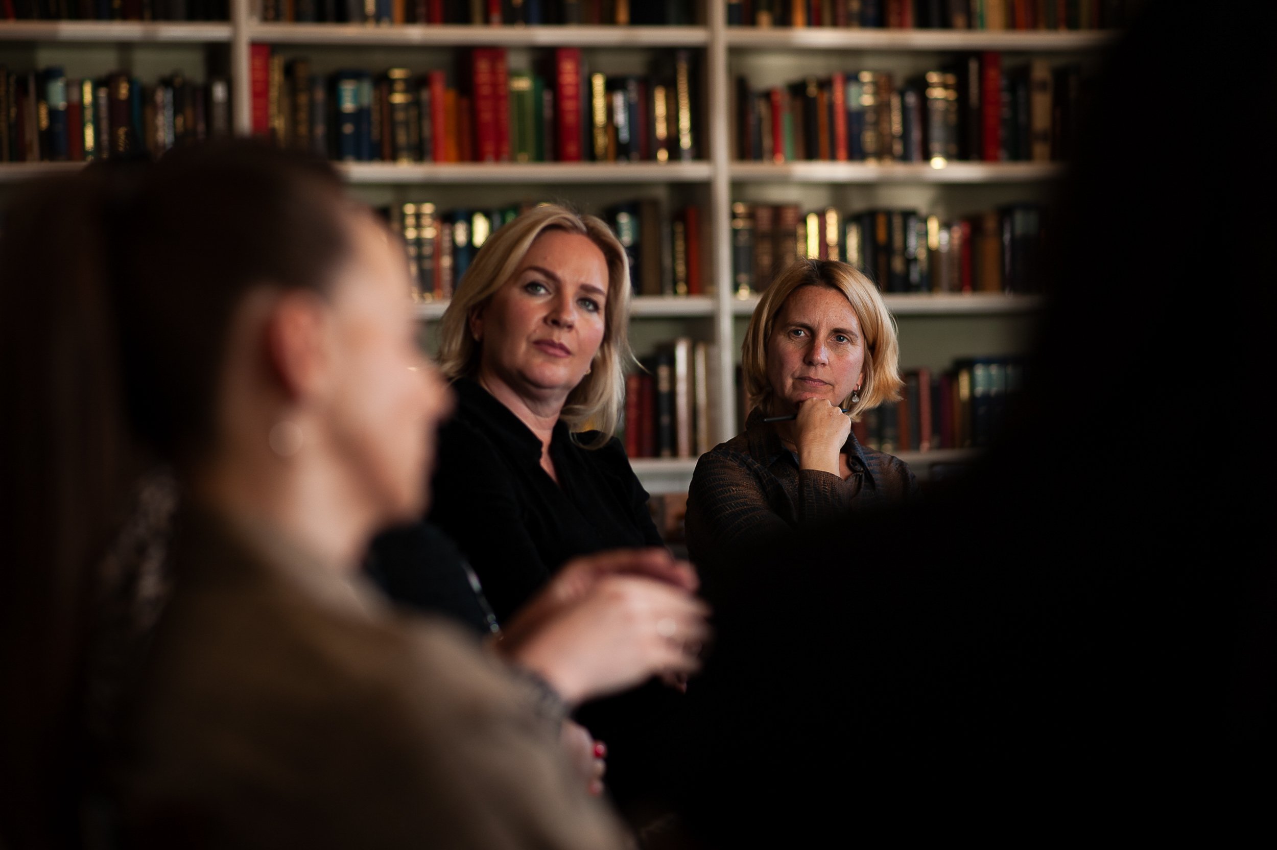 Group of people engaged in discussion, sitting in front of bookshelves.