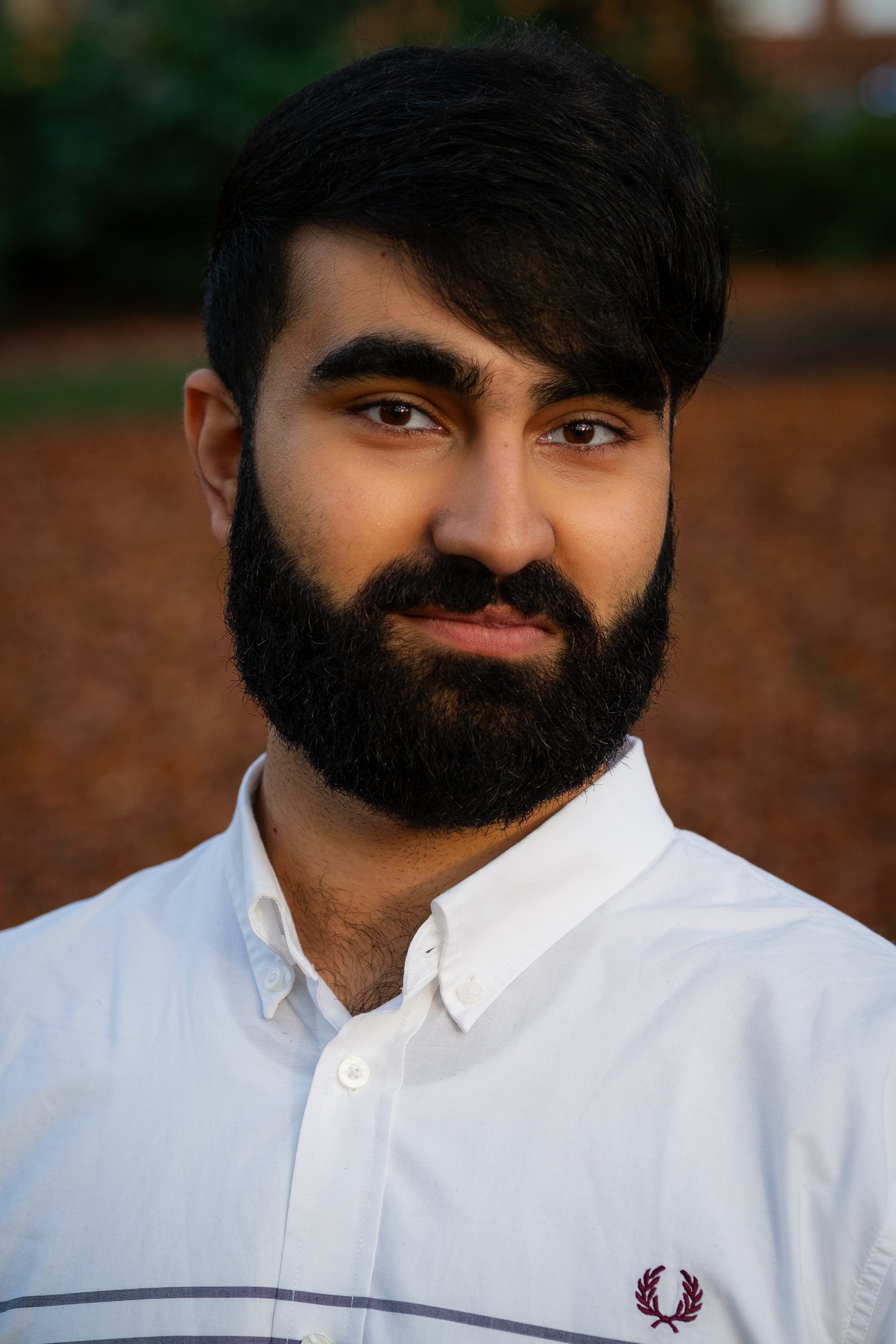 Portrait of a man with a beard wearing a white shirt, standing outdoors.