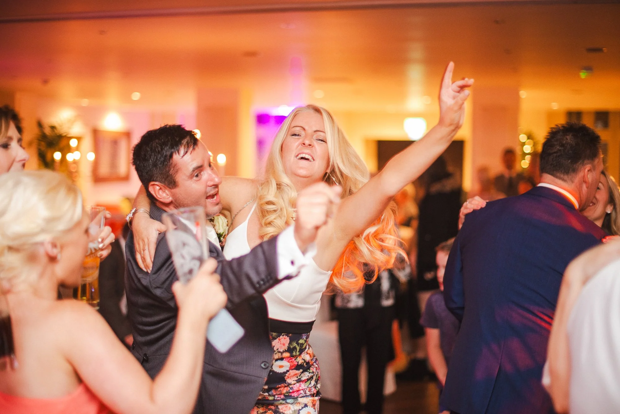 People dancing and celebrating at a lively party or wedding reception, with colorful lighting and joyful expressions.