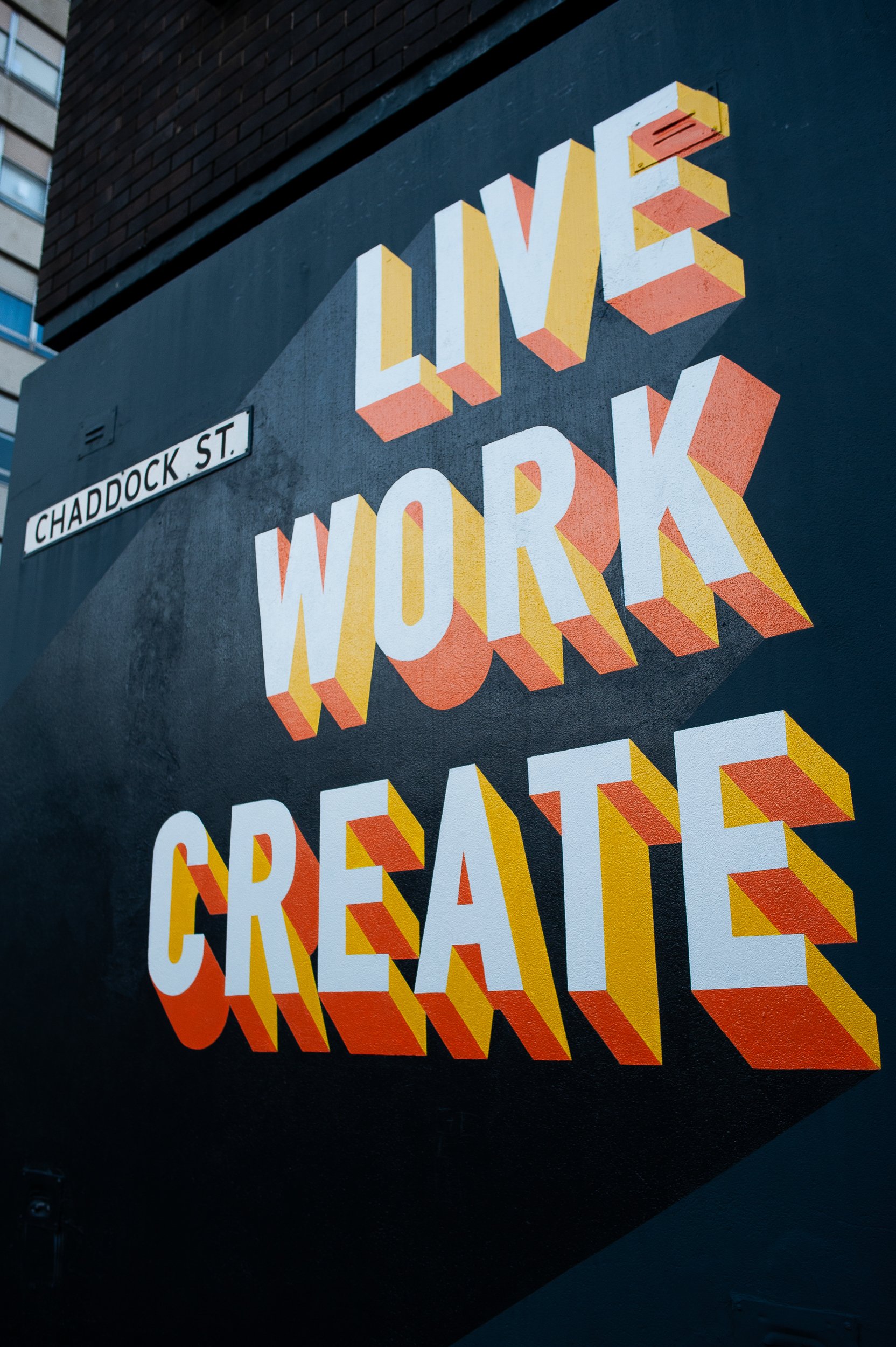 Street art with the words "Live Work Create" on a building, with a street sign reading "Chaddock St."