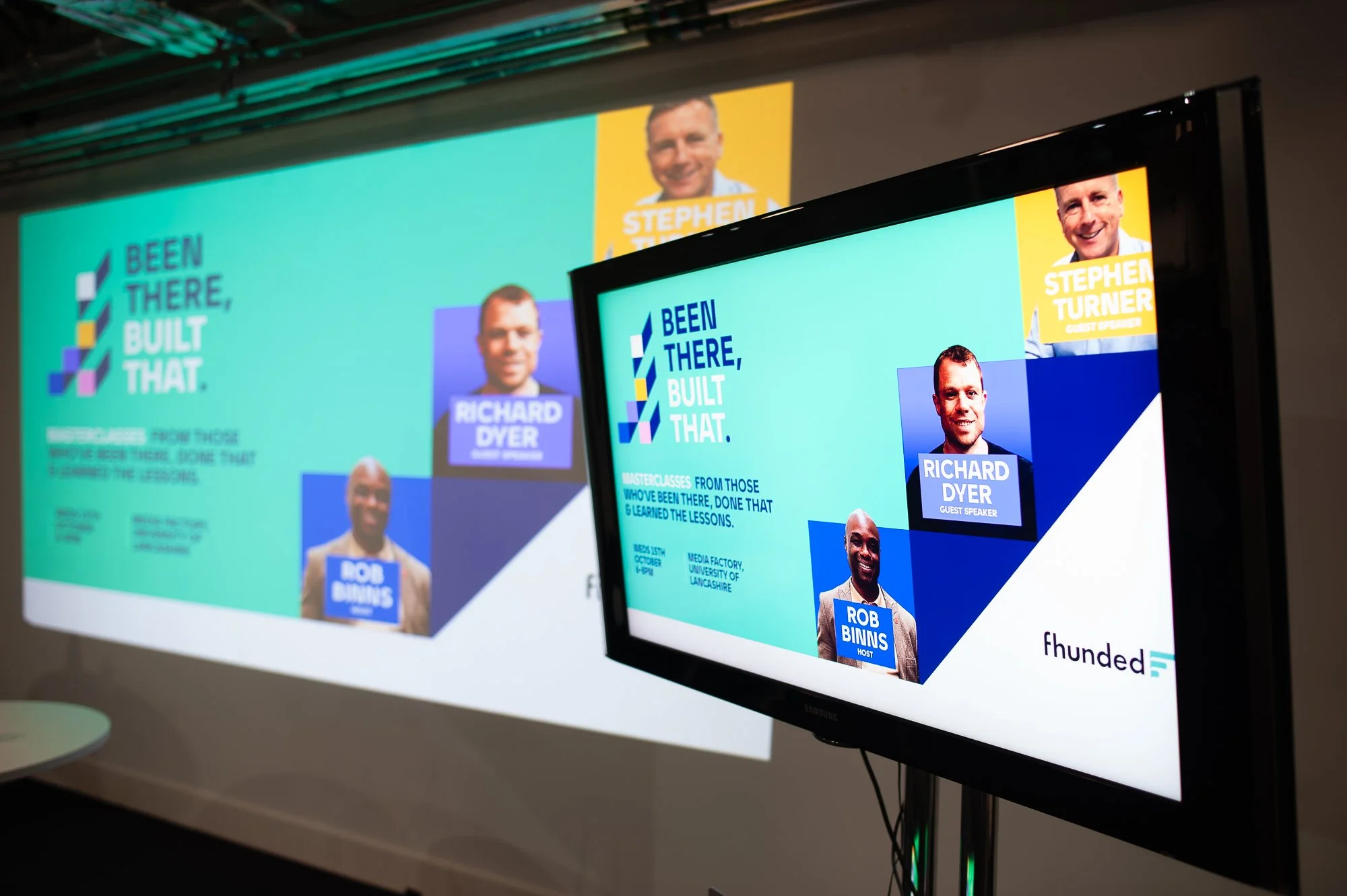 A presentation slide shown on a projector screen and a TV monitor at a conference, featuring portraits and names of speakers. The slide reads 'Been There, Built That' in large text, with names Richard Dyer, Rob Binns, and Stephen Turner, each with th