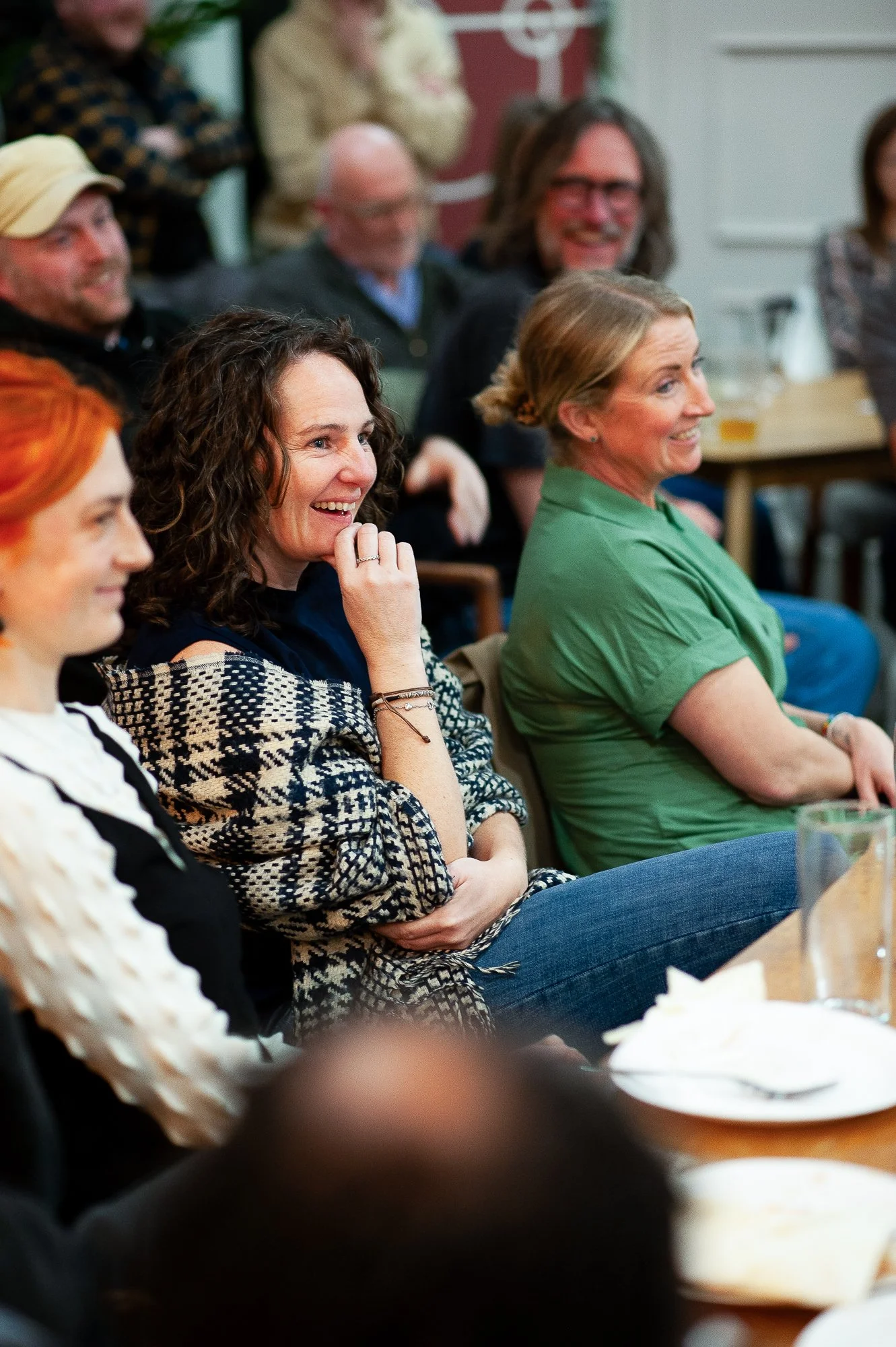 A group of smiling people seated at a table in a social setting, enjoying a moment of laughter.