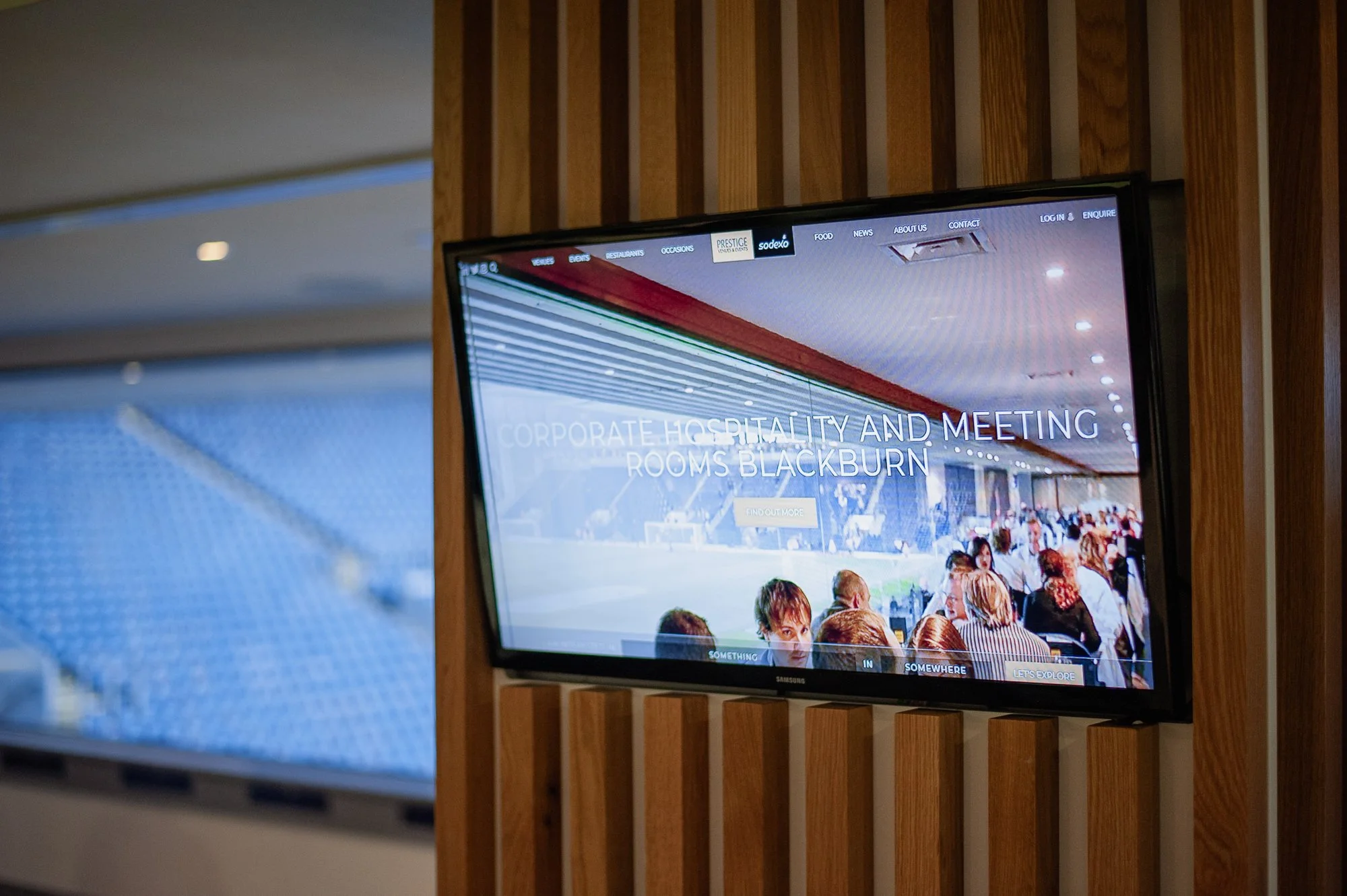 Television screen displaying information about corporate hospitality and meeting rooms in Blackburn, mounted on a wooden wall