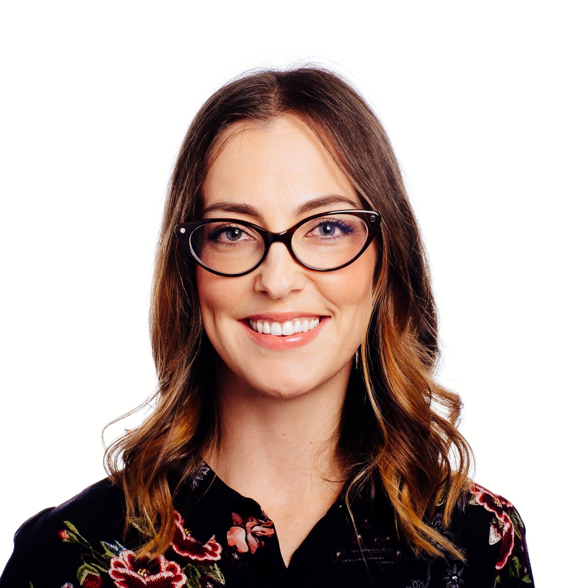 Smiling woman with brown hair and glasses wearing a floral blouse.