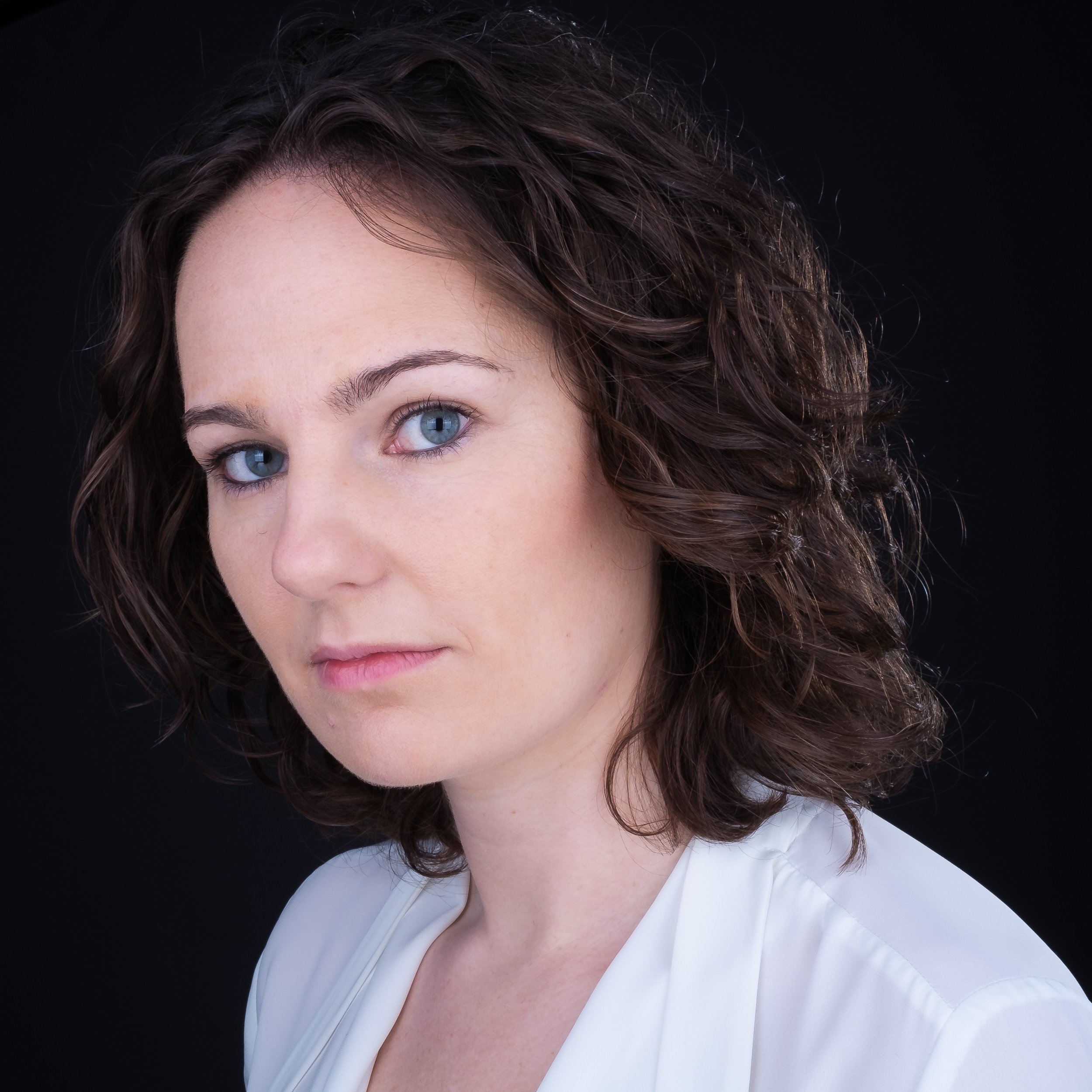 Woman with brown curly hair and blue eyes against black background