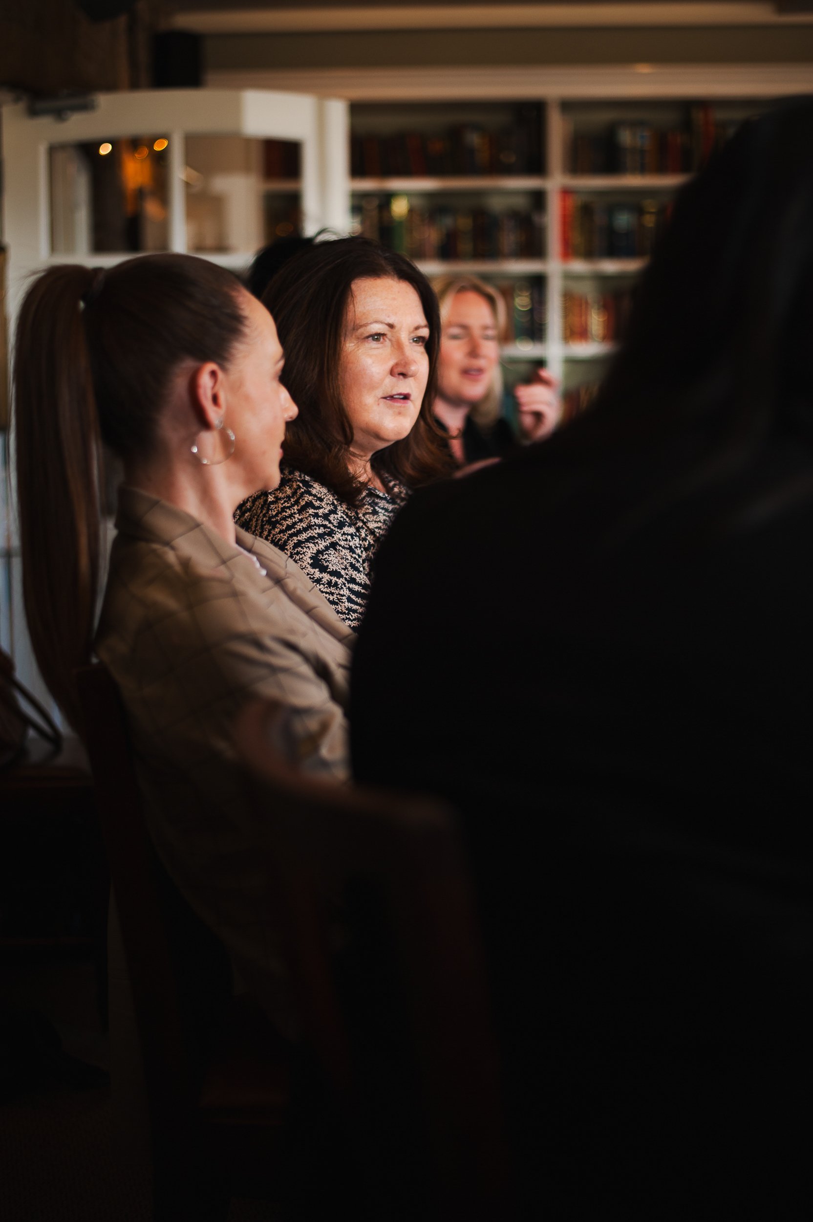 Group of people sitting in a room with bookshelves, engaged in conversation.