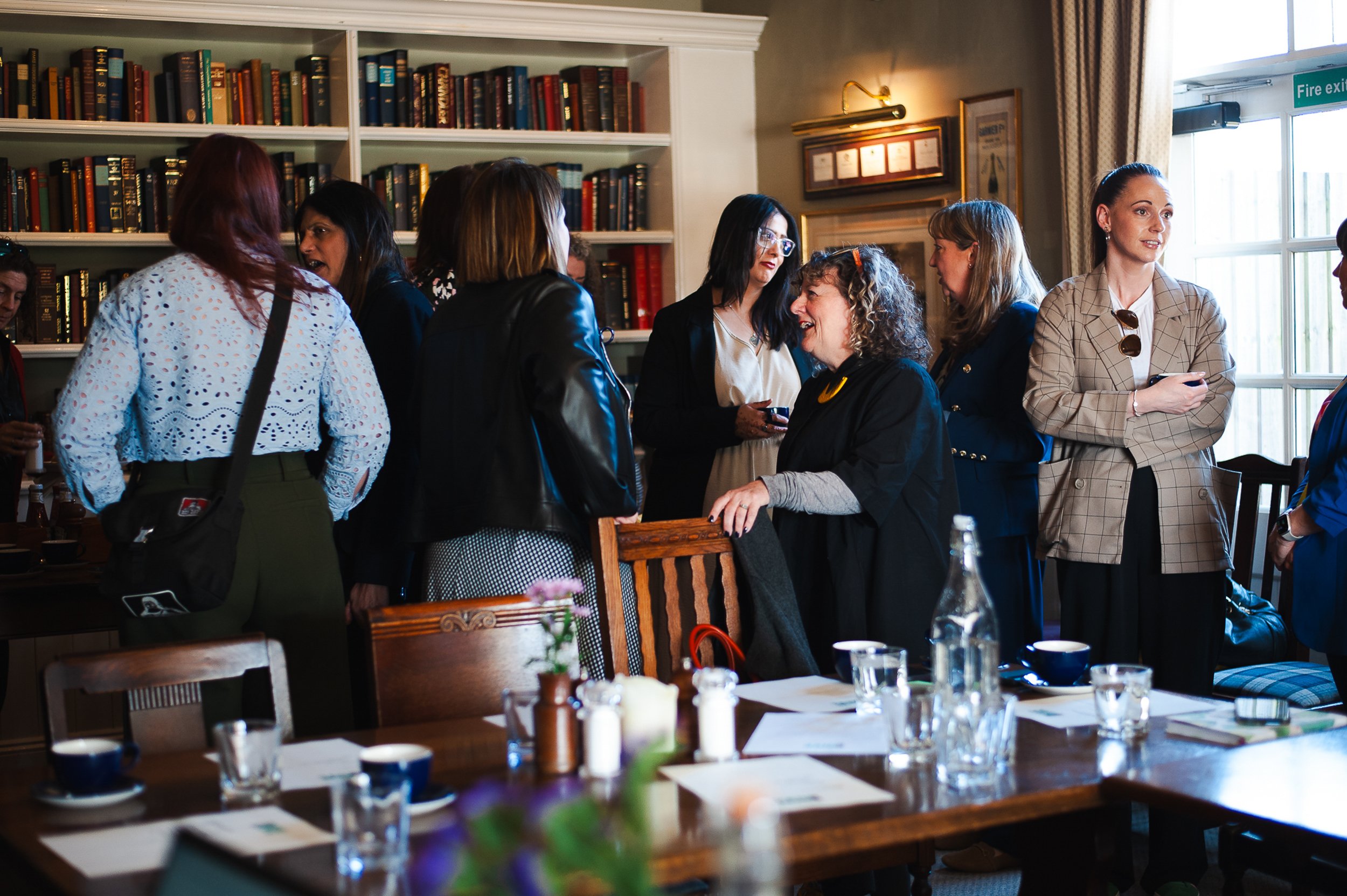 Group of people socializing in a room with bookshelves and wooden table