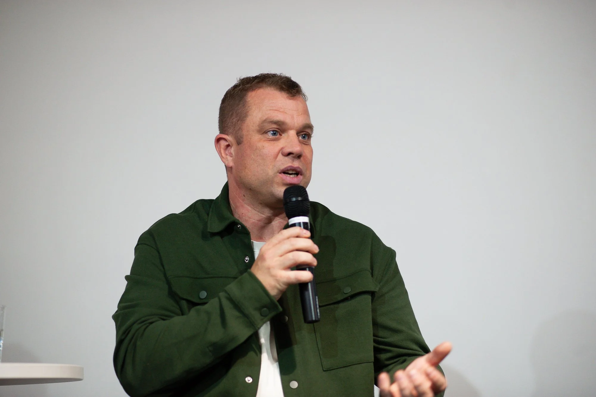 A man with short brown hair wearing a green jacket speaking into a microphone.