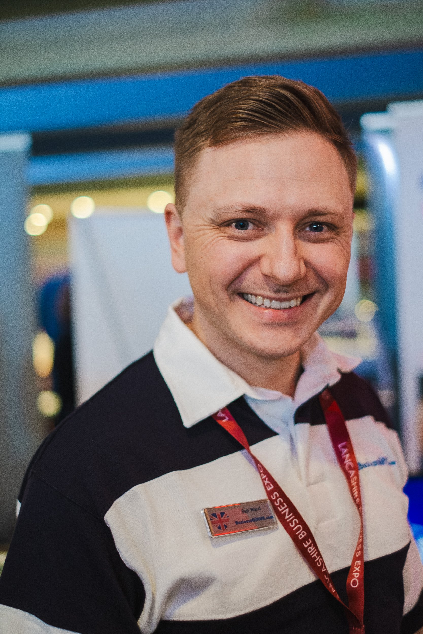 Smiling man at event wearing striped shirt and name badge.