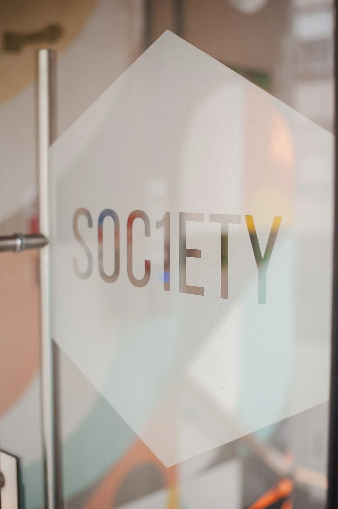 Close-up of a glass door with the word 'SOCIETY' written on it in frosted letters, with a modern interior space visible in the background.