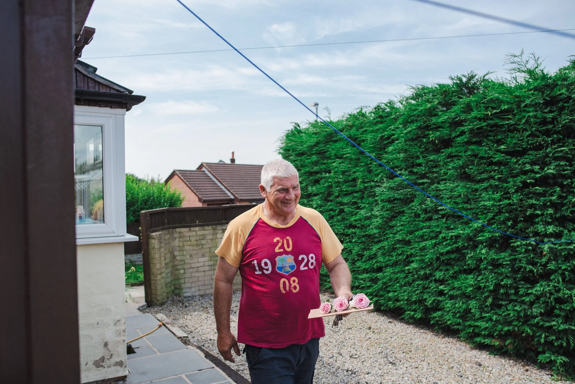A man with gray hair smiling and holding a tray with pink roses in a backyard.