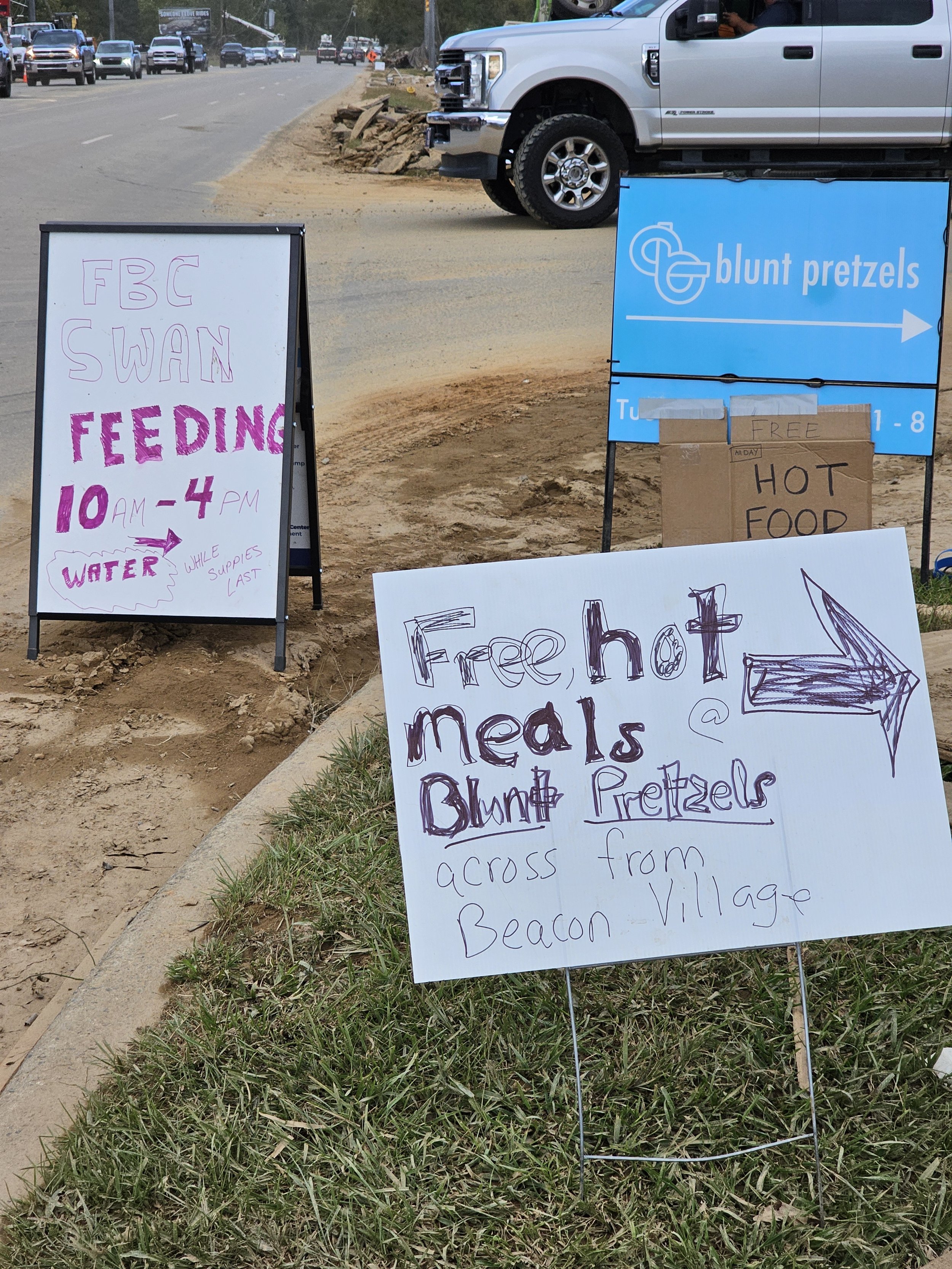 Signs advertising free hot meals and pretzels, with serving hours from 10 AM to 4 PM, and a sign indicating free hot food across from Beacon Village.