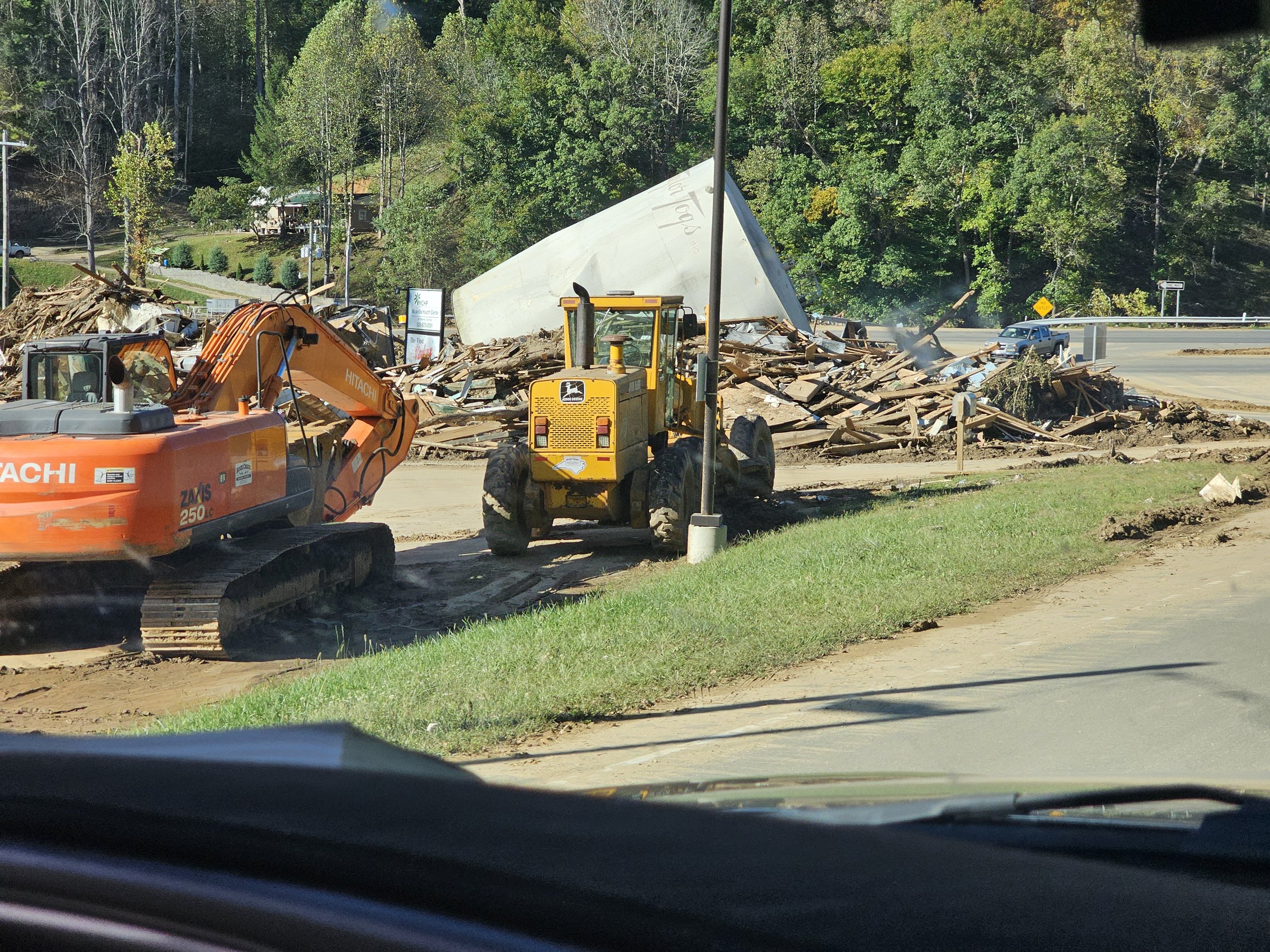 Road construction site with excavator and bulldozer clearing debris from a collapsed building near a roadside.