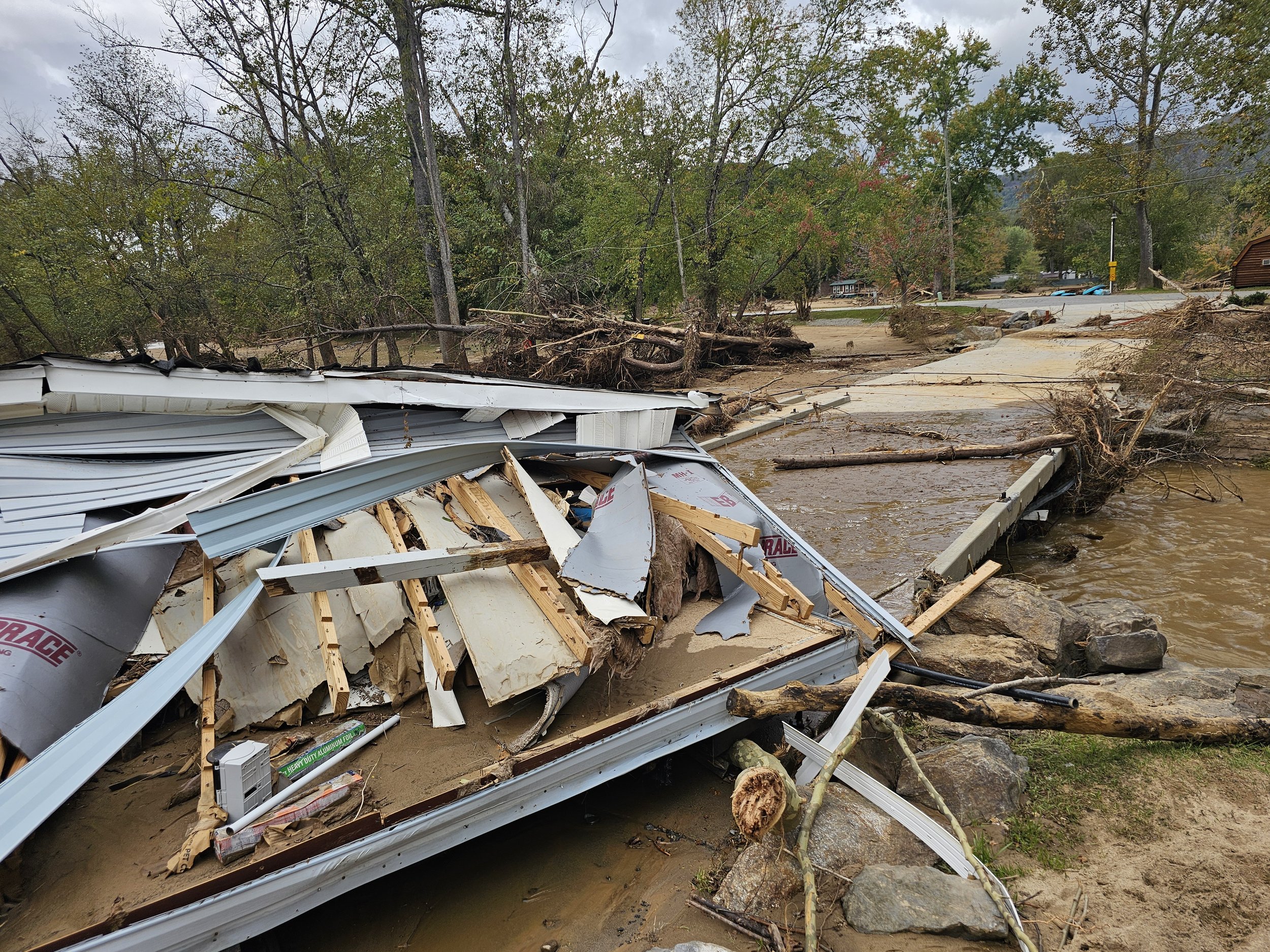 Debris and damaged structure from a flood, with fallen trees, mud, and scattered materials in a rural area.