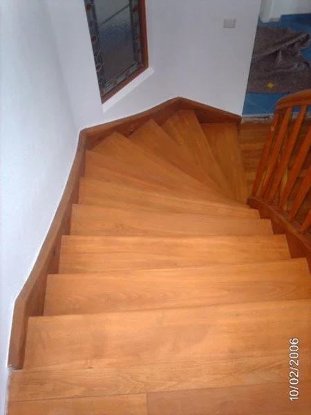 Holztreppe mit geformtem Geländer, Blick nach oben Richtung Obergeschoss.