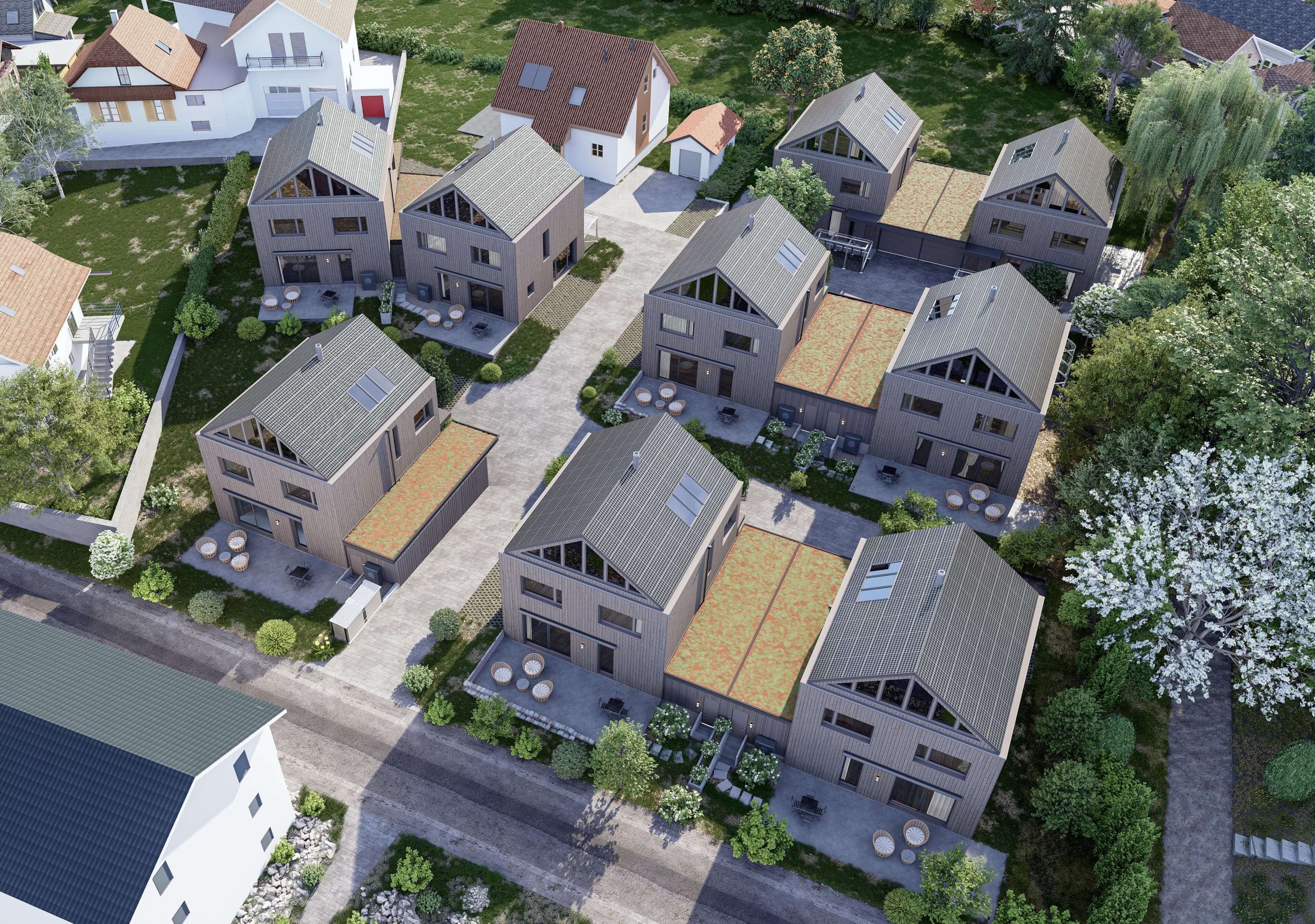 Luftaufnahme eines modernen Wohnquartiers mit mehreren zweistöckigen Häusern, umgeben von Bäumen und Wegen, einige Dächer mit Solarpanelen, private Terrassen mit Gartenmöbeln und begrünten Flächen.