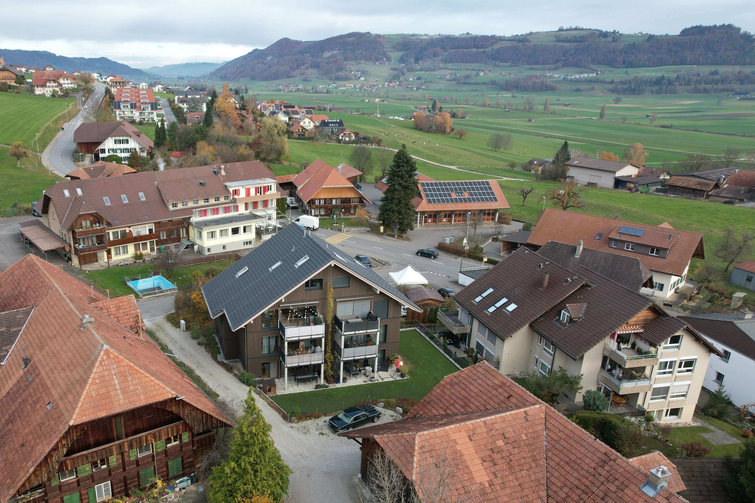 Blick auf eine kleine Stadt im Grünen mit Mehrfamilienhäusern, Einfamilienhäusern, Straßen und umliegender Natur.