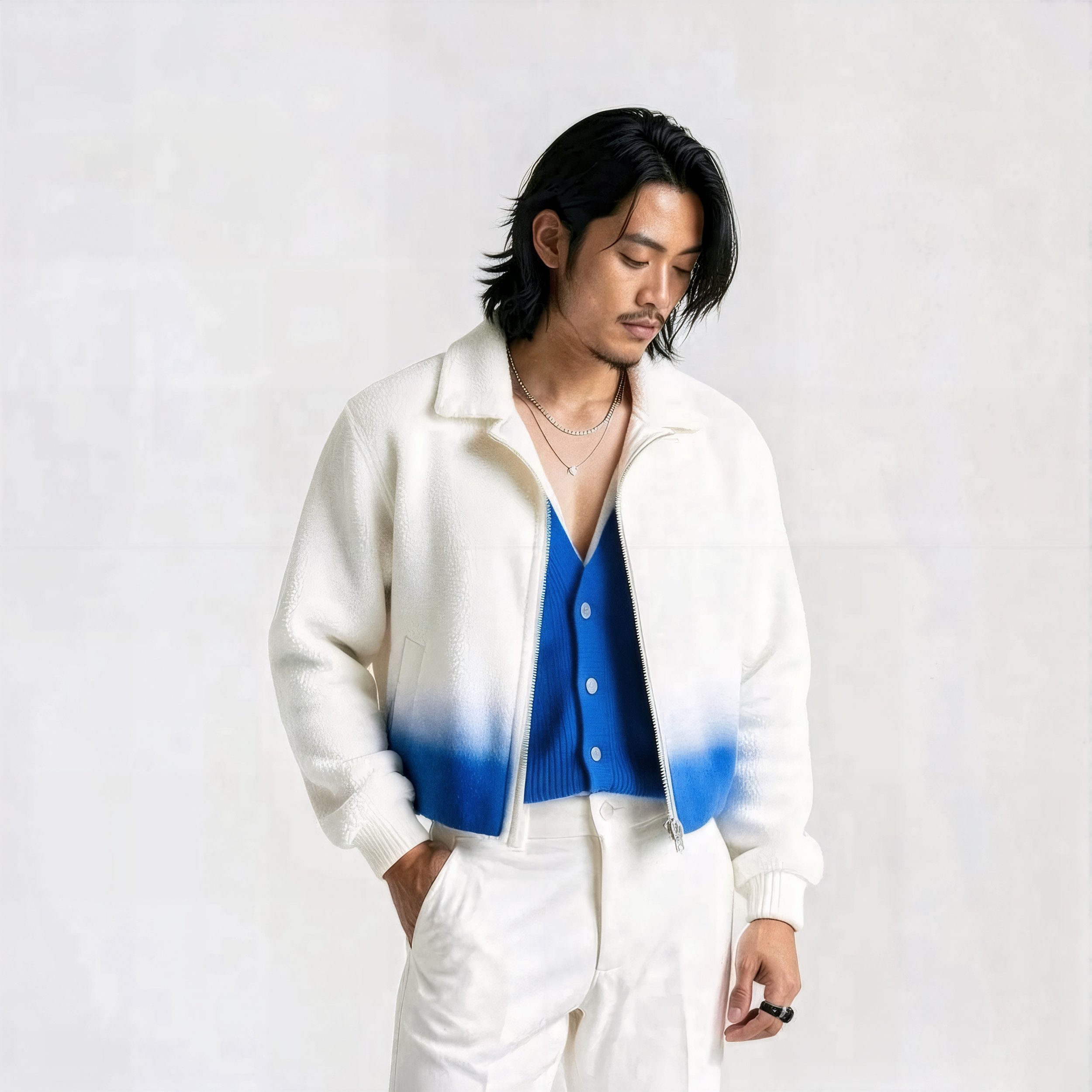 Man with long black hair wearing a white zip-up jacket over a blue button-up shirt, with white pants, standing against a plain white background.