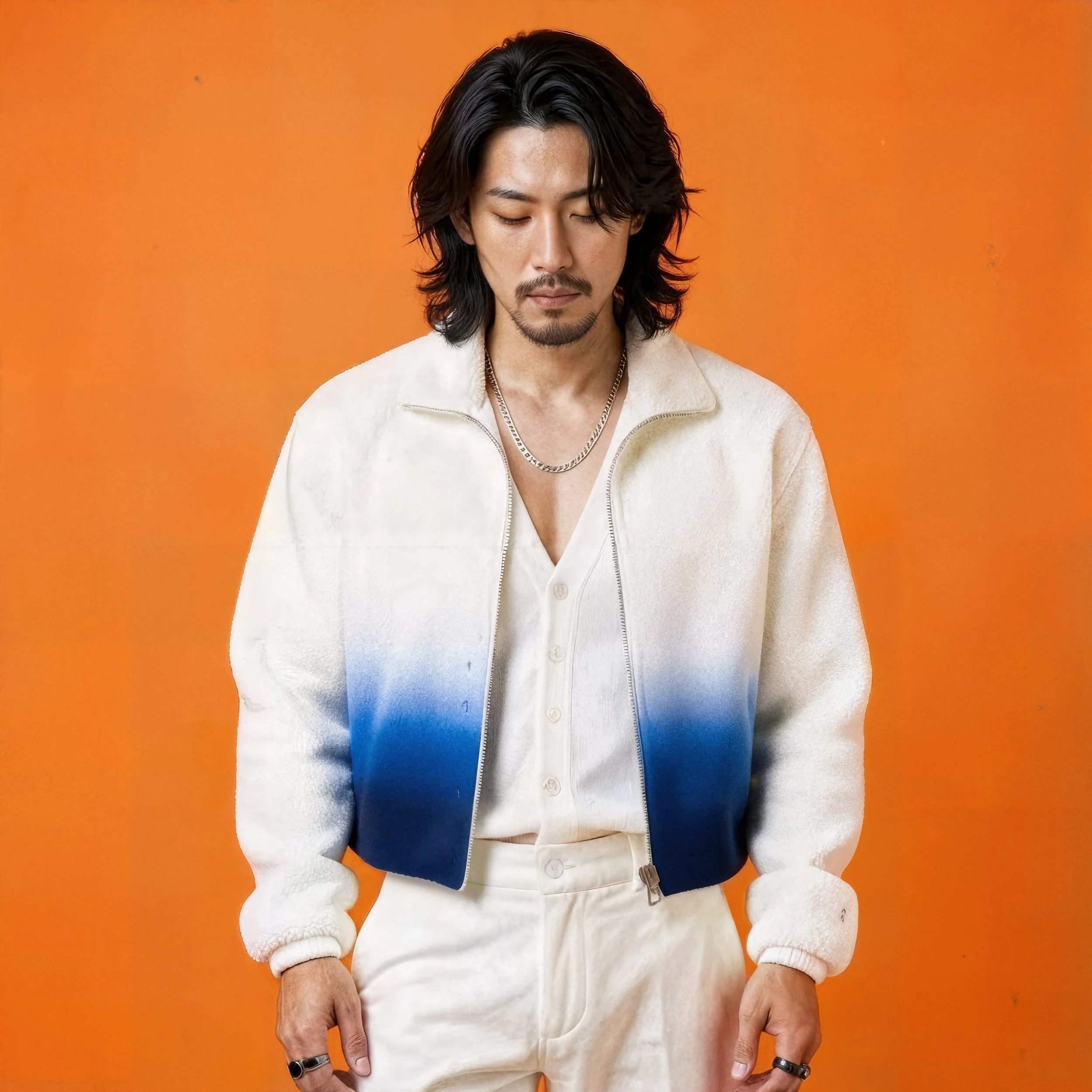 Man with long black hair, a mustache, and goatee wearing a white and blue gradient jacket, white shirt, and cream pants, standing against an orange background.