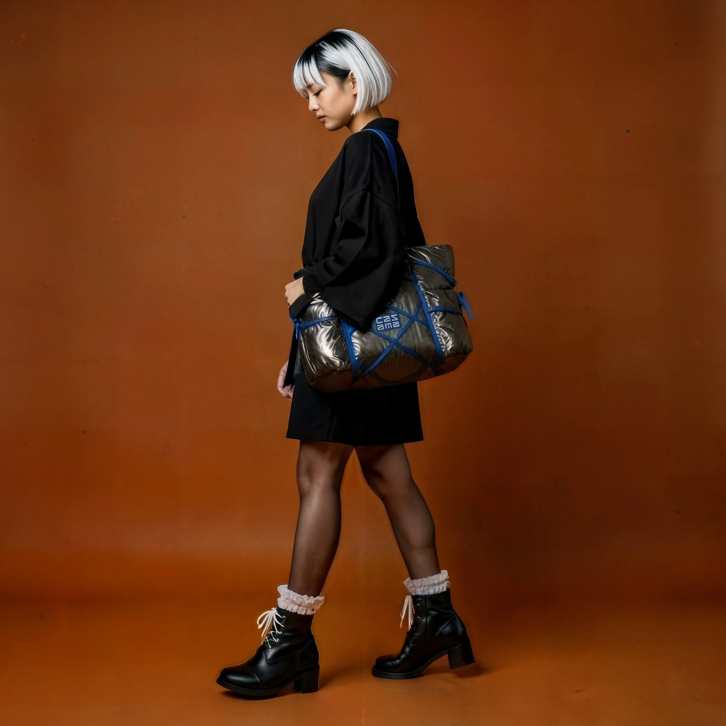 A woman with short, black and white hair, wearing a black outfit with sheer black tights, beige sock cuffs, and black heeled boots. She carries a large, metallic gray rolled-up bag with blue straps and stands against a brown background, looking down.