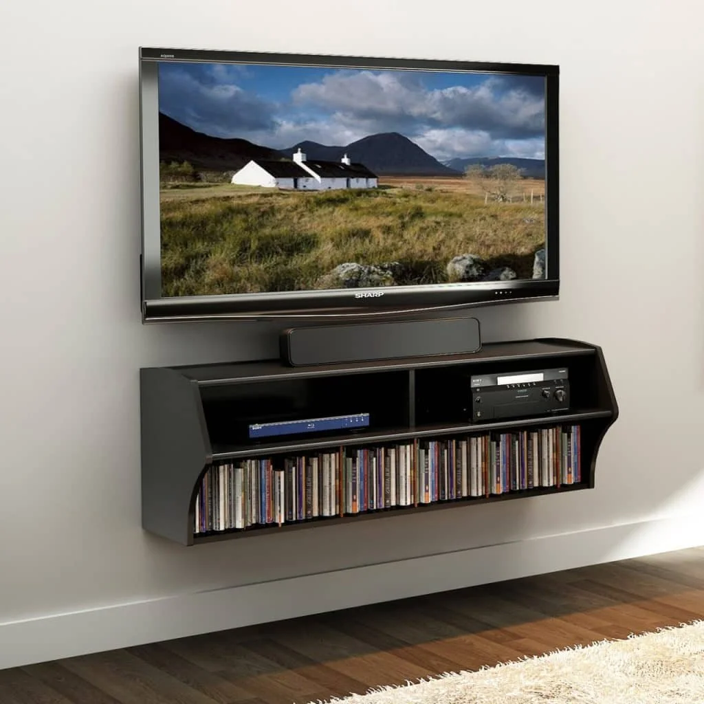 Flat-screen TV mounted on a wall displaying a landscape with mountains and a house, with a soundbar beneath it and a shelf below holding CDs, a DVD player, and a stereo receiver.