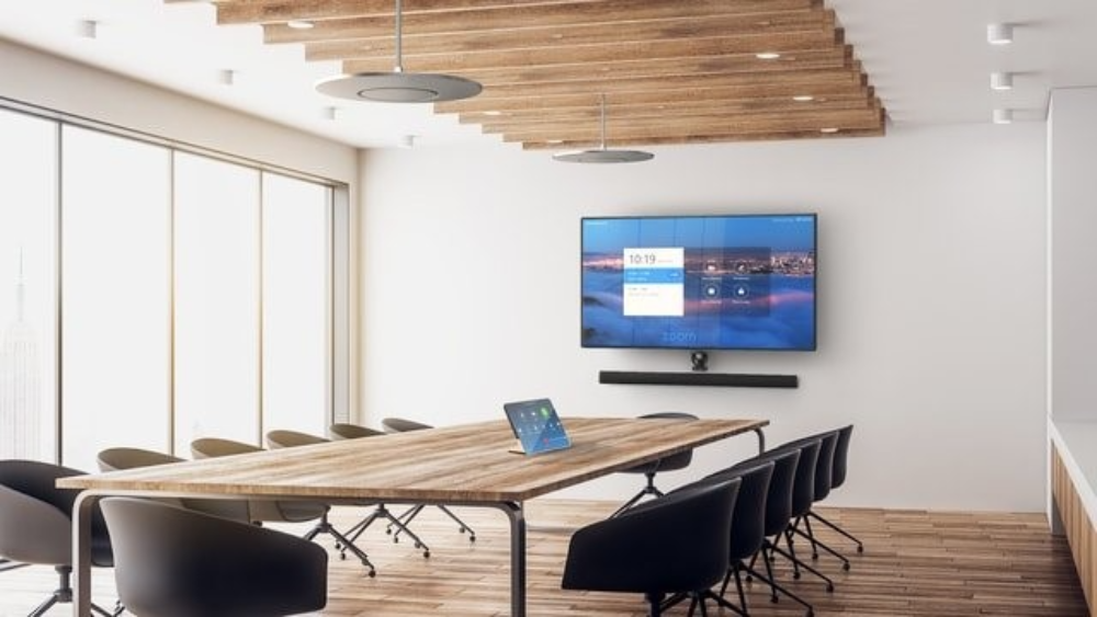 Modern conference room with a large wooden table, black chairs, large windows, a wall-mounted screen, and wooden ceiling decor.