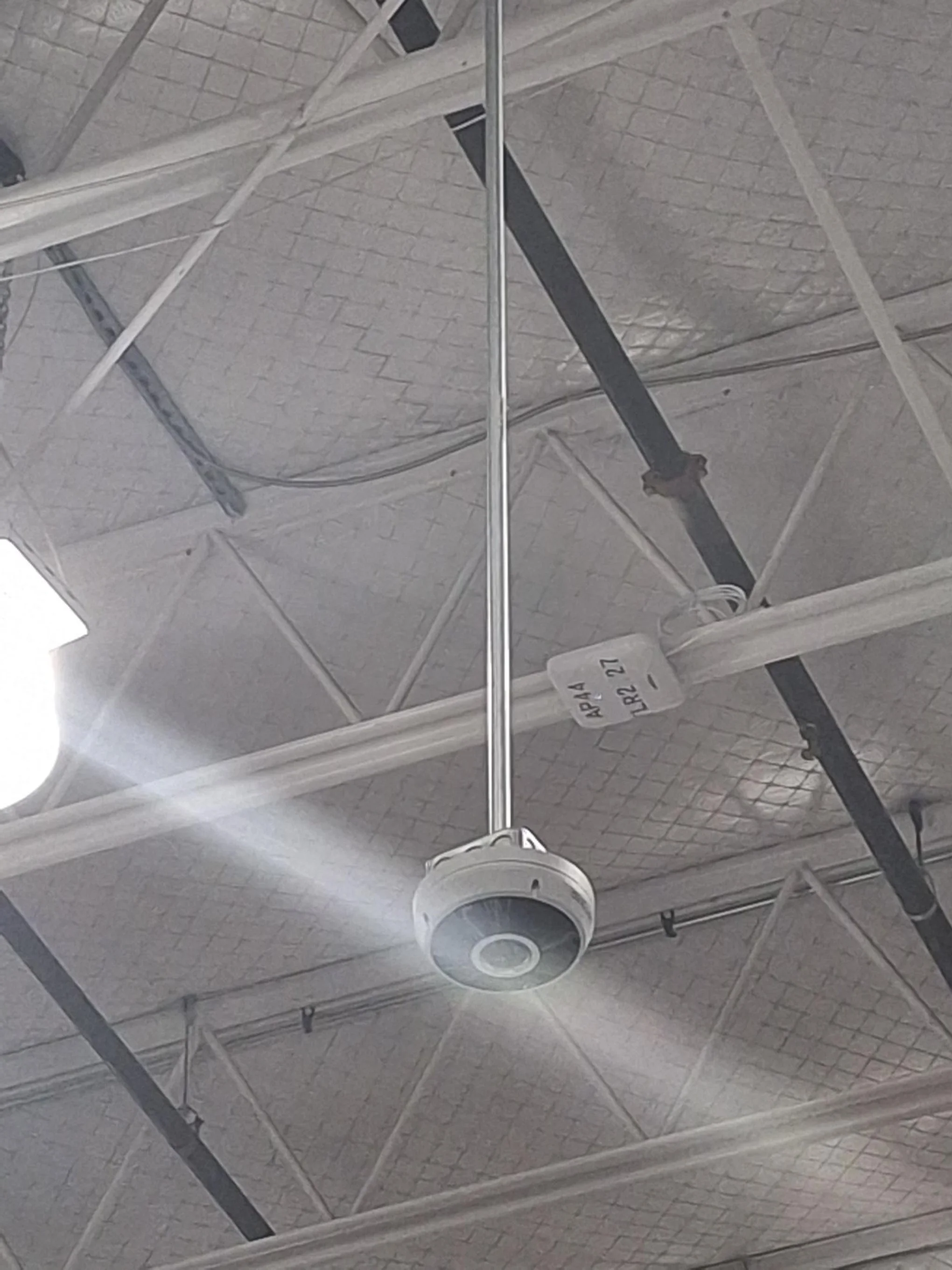 Ceiling of an airport or large building with a surveillance camera hanging from the ceiling.