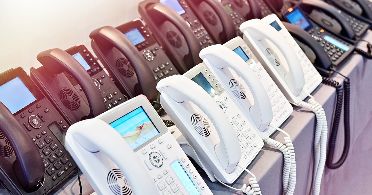 A row of landline telephones on a table, with white and black phones visible.