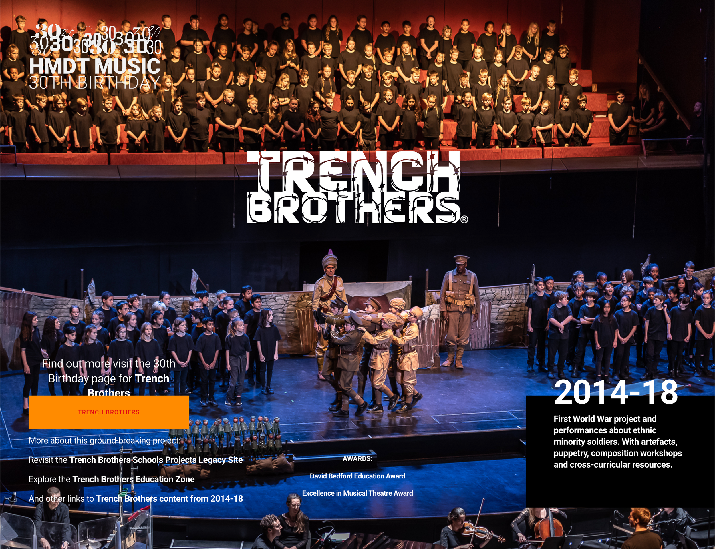 A stage filled with children and performers dressed in costumes, with an audience watching in the foreground. The scene appears to be from a theatrical performance about the Trench Brothers, with banners and text referencing the 30th birthday and projects related to World War I history.