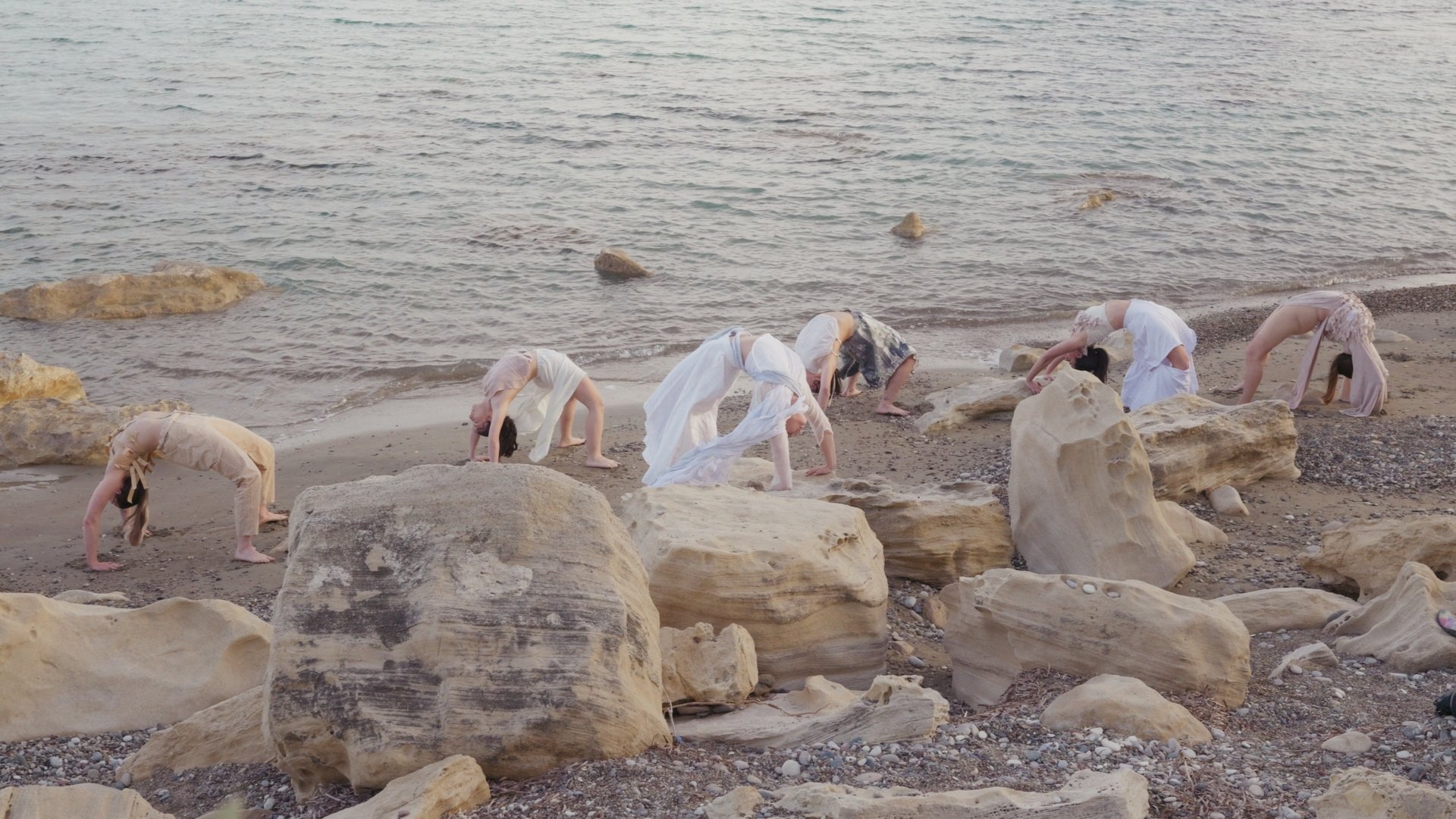 People performing backbend poses on a rocky beach, near the shoreline.