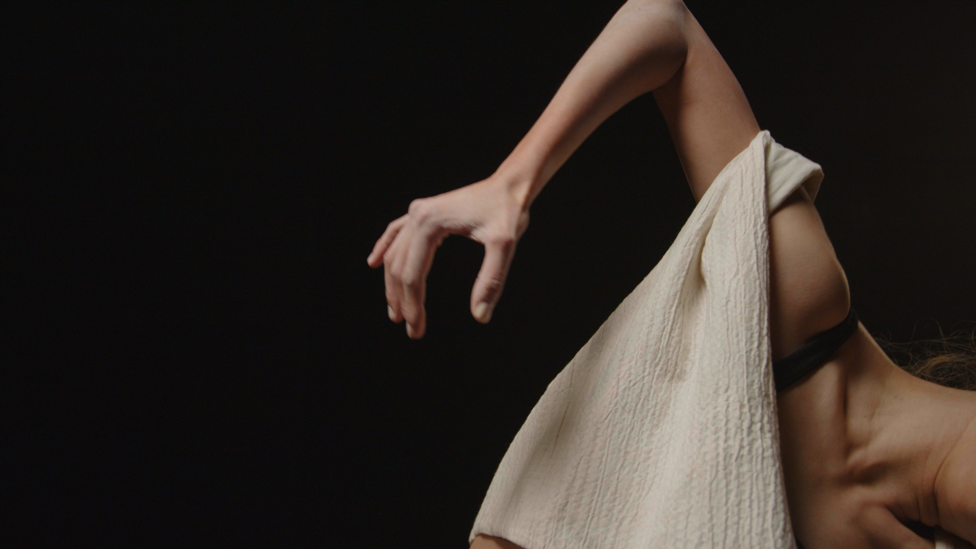 Close-up of an arm extending outward with a white textured fabric draped over the shoulder against a dark background.