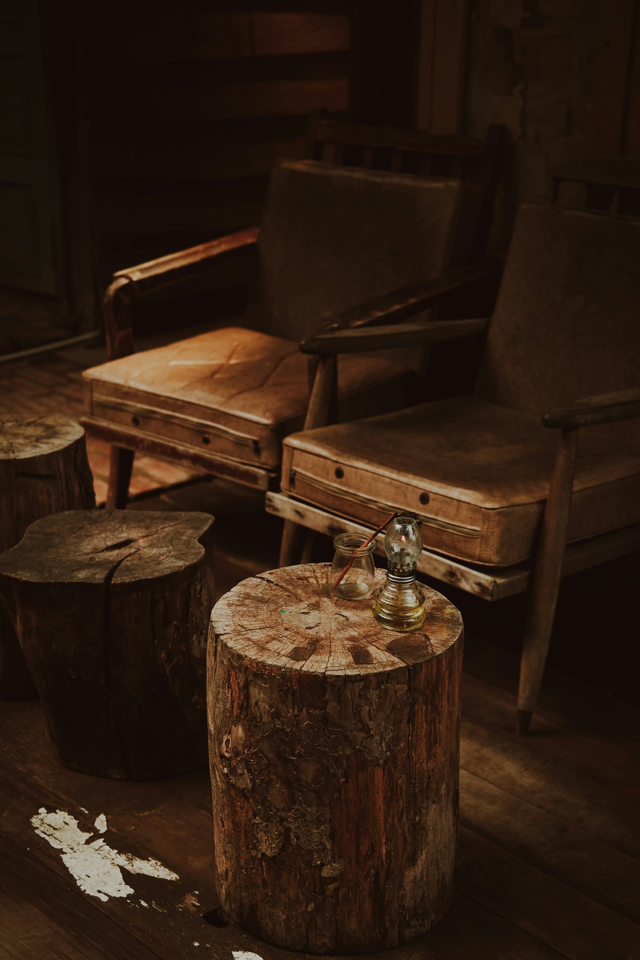 A cozy room with two vintage armchairs, wooden logs used as tables, and a dim warm light.