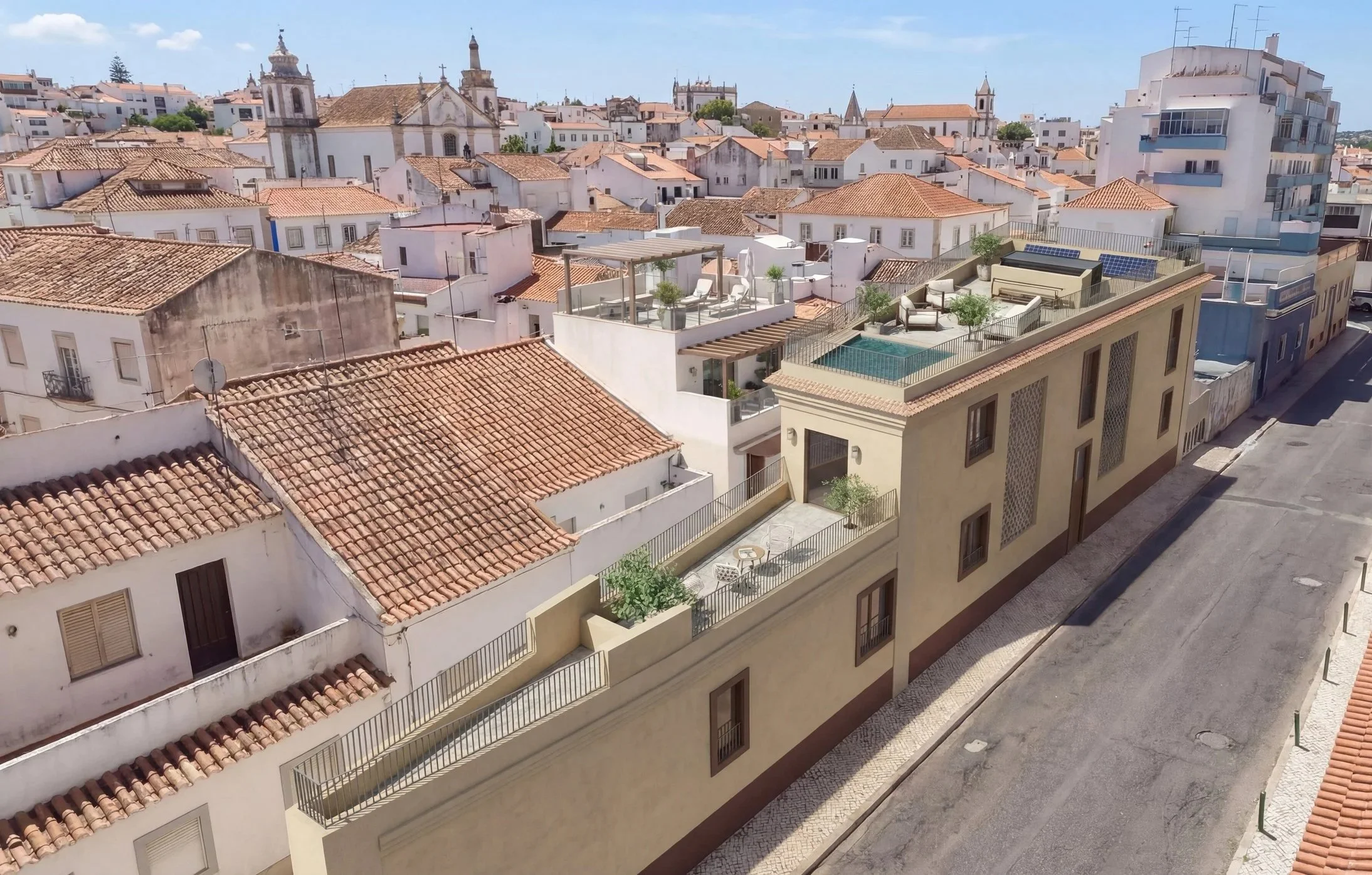 An aerial view of a Mediterranean city with white buildings, terracotta rooftops, and a mix of traditional and modern architecture, including a building with a rooftop pool and outdoor seating area.