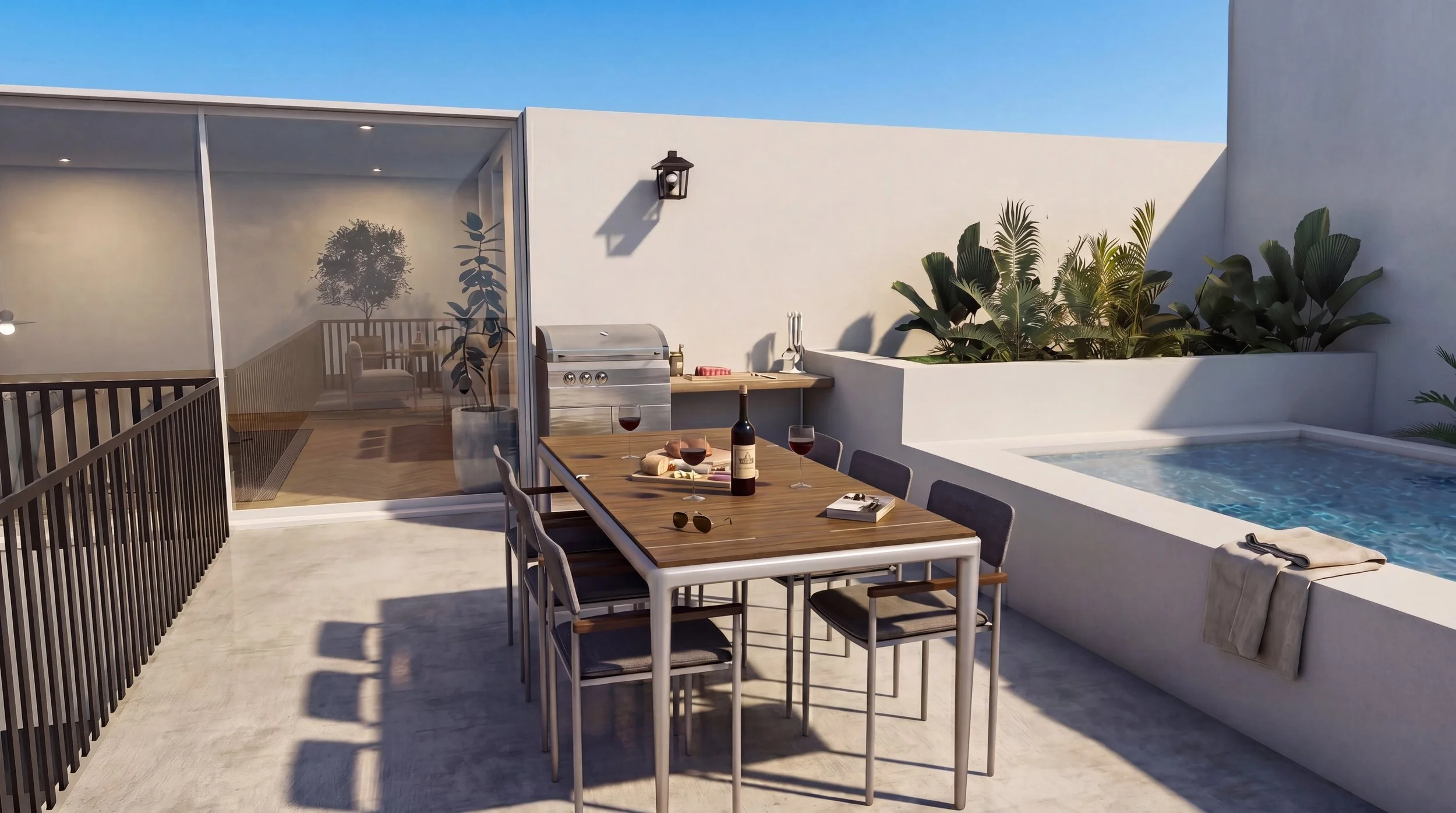 A modern outdoor patio area with a dining table set for a meal, including a bottle of red wine and glasses, next to a small pool or hot tub, with lush plants and a glass-enclosed lounge area in the background on a sunny day.
