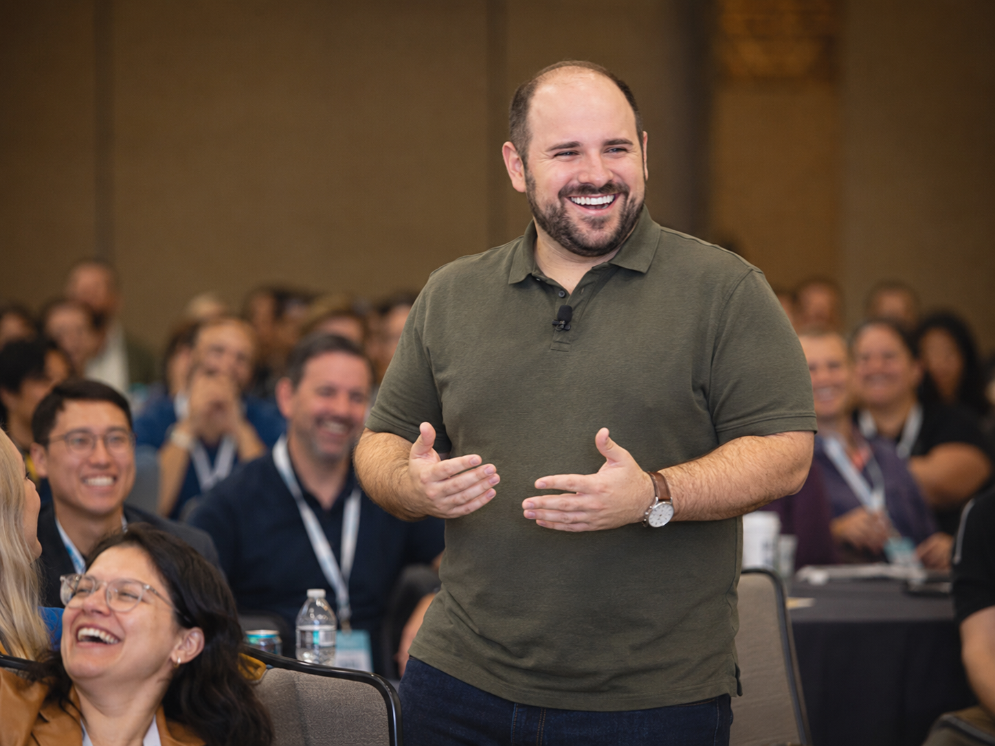 A man standing and smiling in front of seated audience members at a conference or seminar.