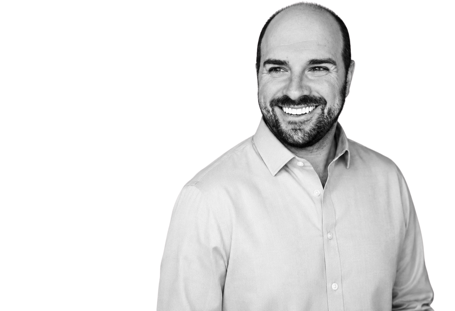 A smiling man with a beard and short hair, wearing a light-colored button-down shirt, looking slightly to the right.