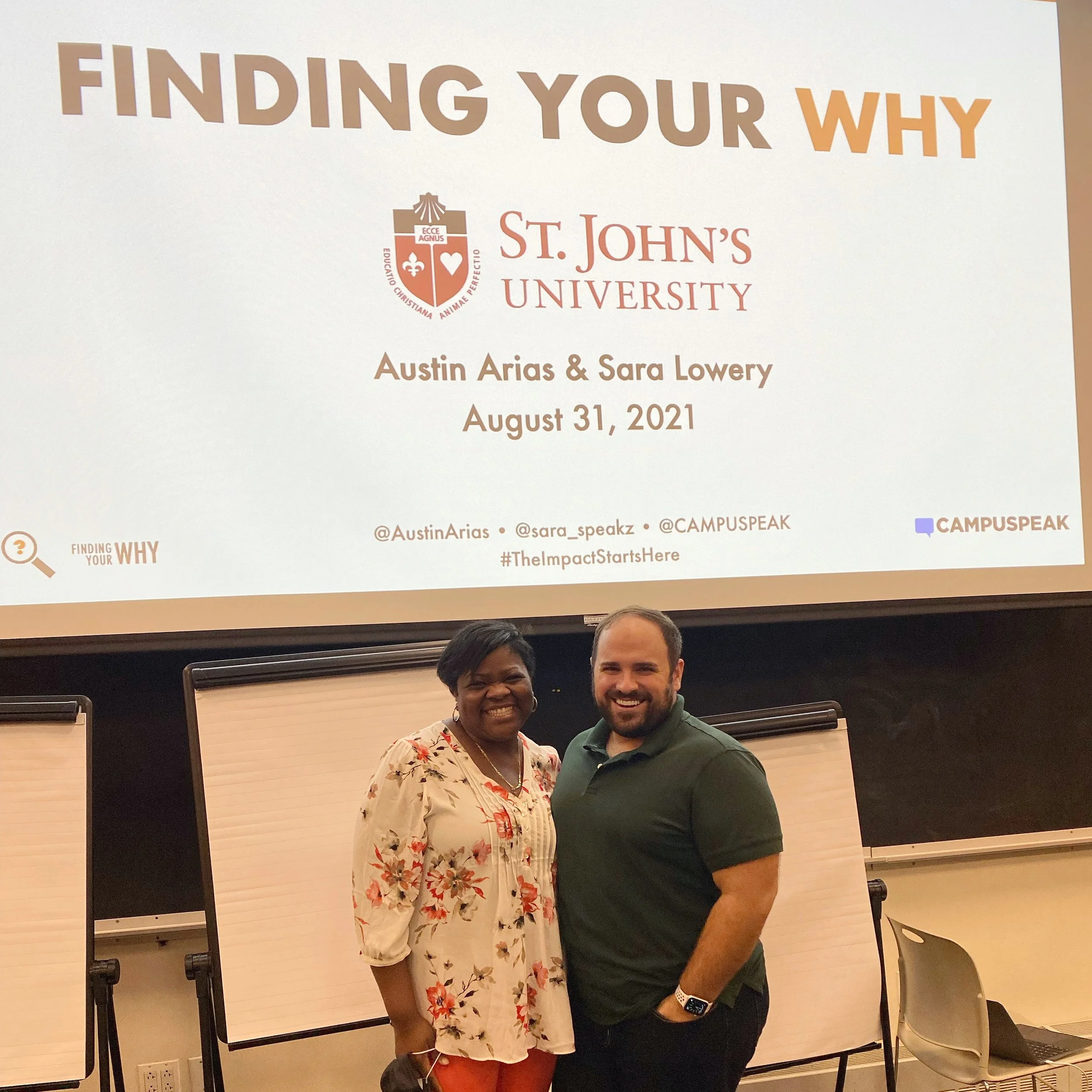 A woman and a man standing in front of a large presentation screen, smiling. The screen displays the title 'Finding Your Why' from St. John's University with event details.
