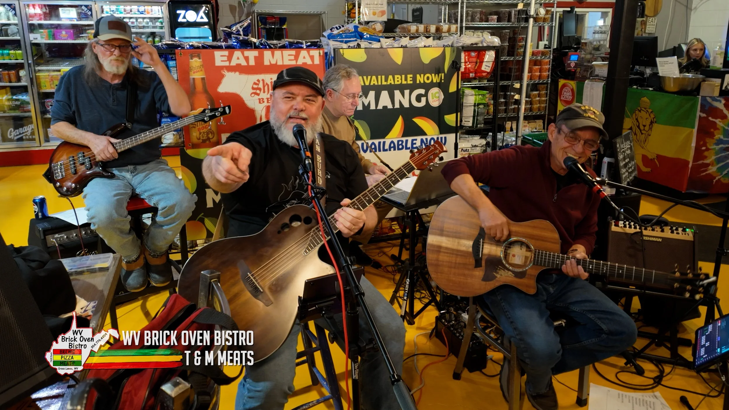 A group of four men performing live music at an indoor venue, with two playing guitars, one playing bass, and one on keyboard, surrounded by colorful signs and merchandise.