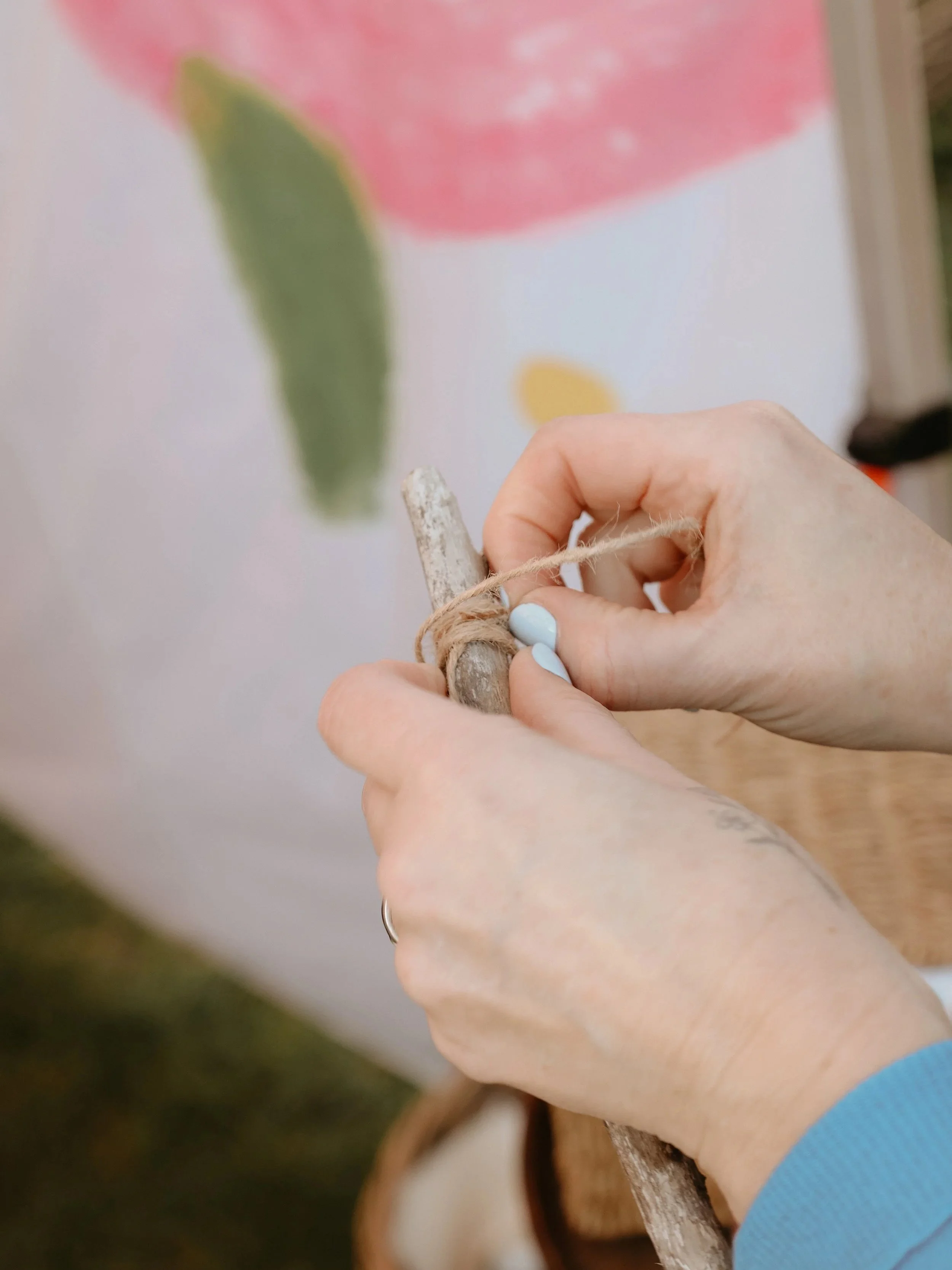 Person tying a piece of twine around a piece of wood, with a blurred colorful background.
