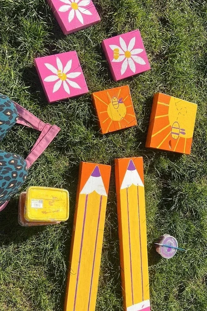 Colorful painted wooden blocks and a small container of yellow paint on grass.