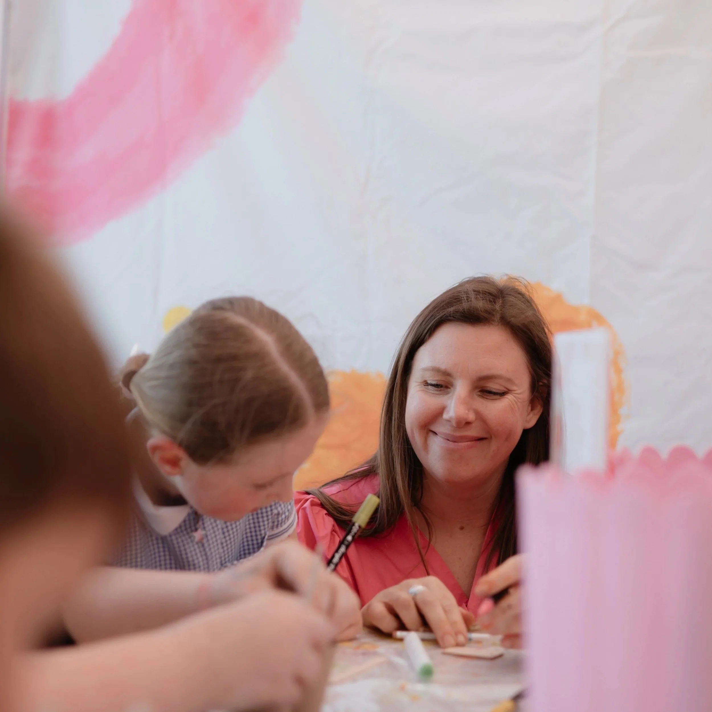 People gathered around a table, drawing or writing with markers, smiling and engaging in a group activity.