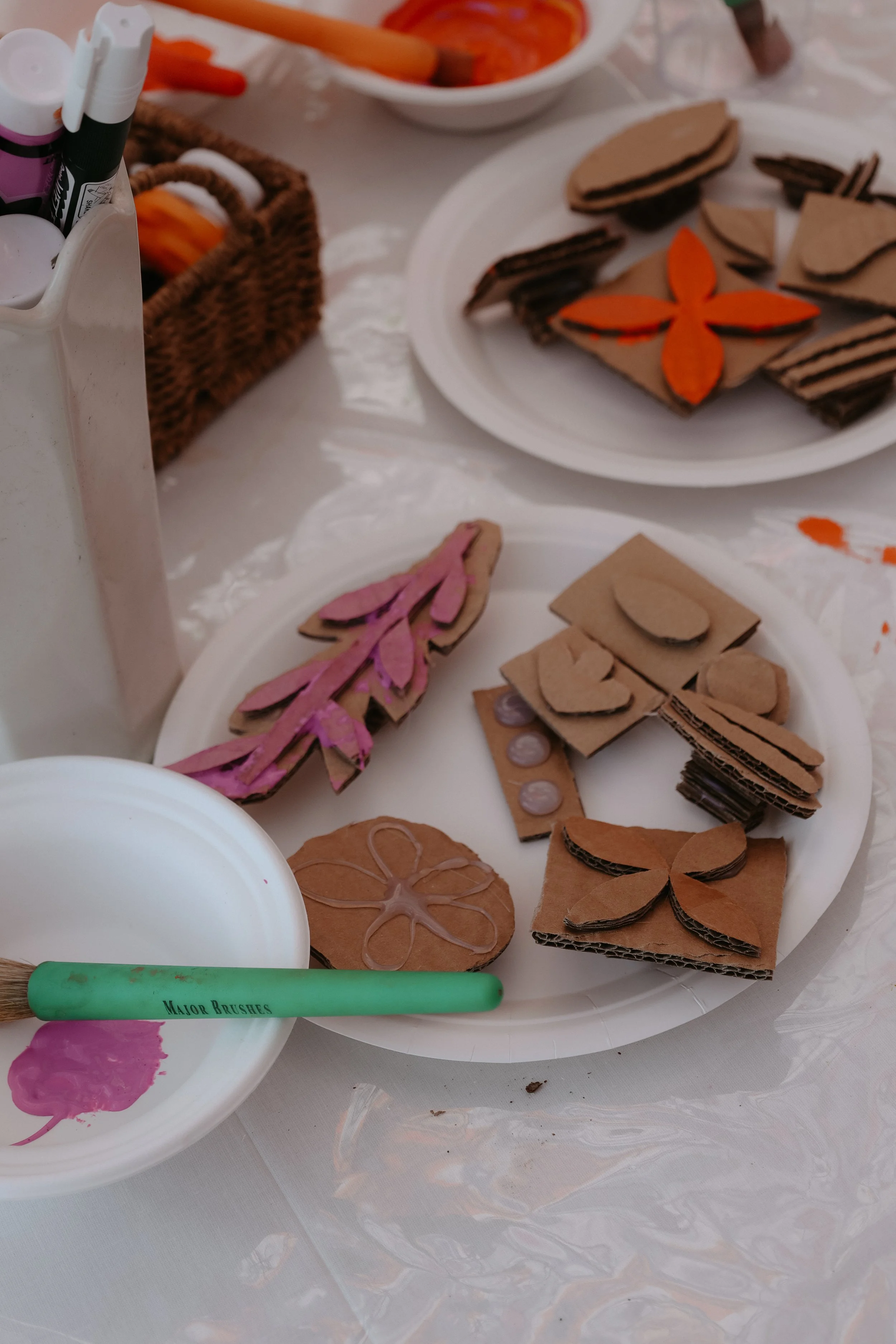 Decorative gingerbread cookies in various shapes, decorated with pink, orange, and brown icing, placed on white paper plates for crafting or baking.